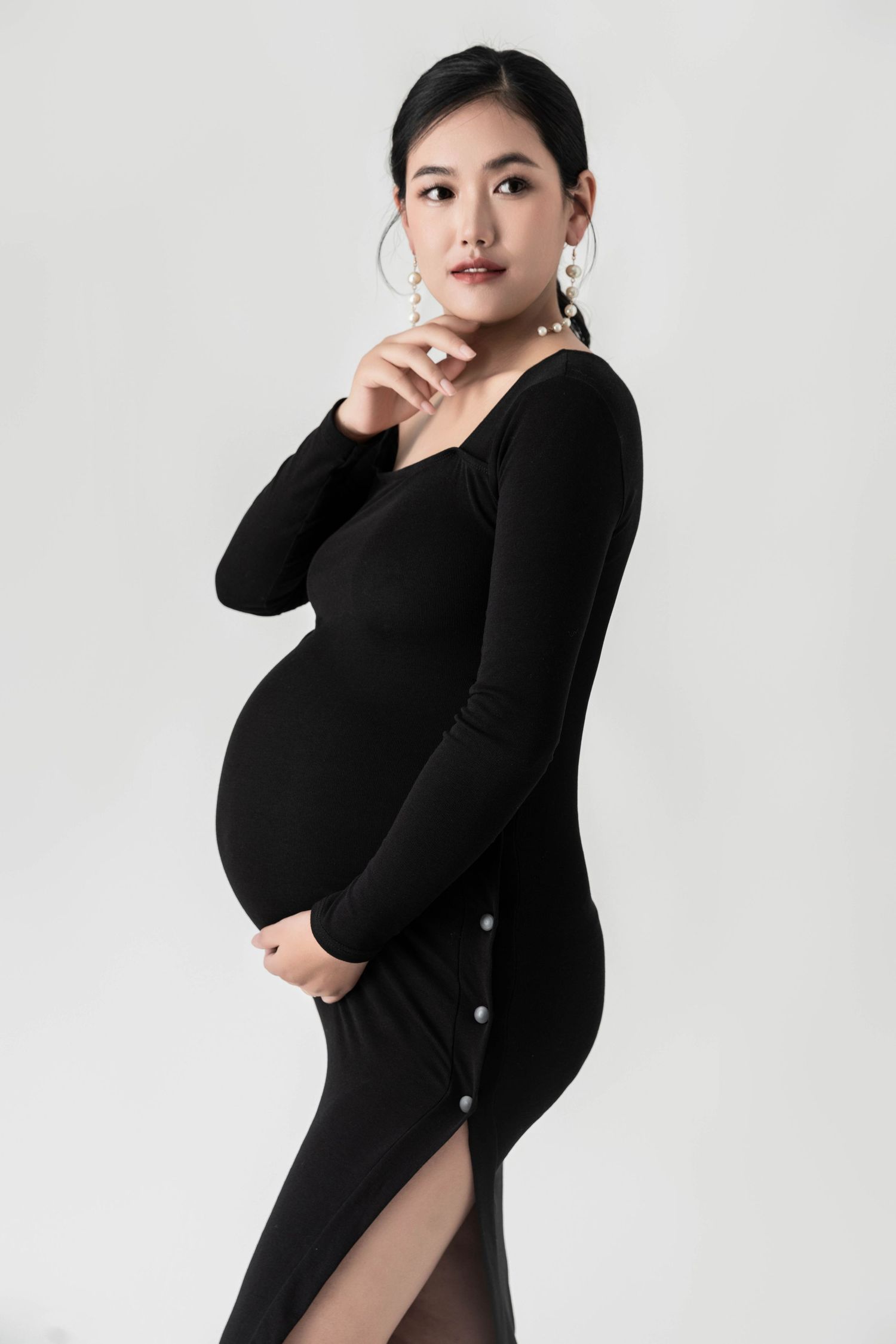 Professional maternity photoshoot series in classic black dress with studio lighting.