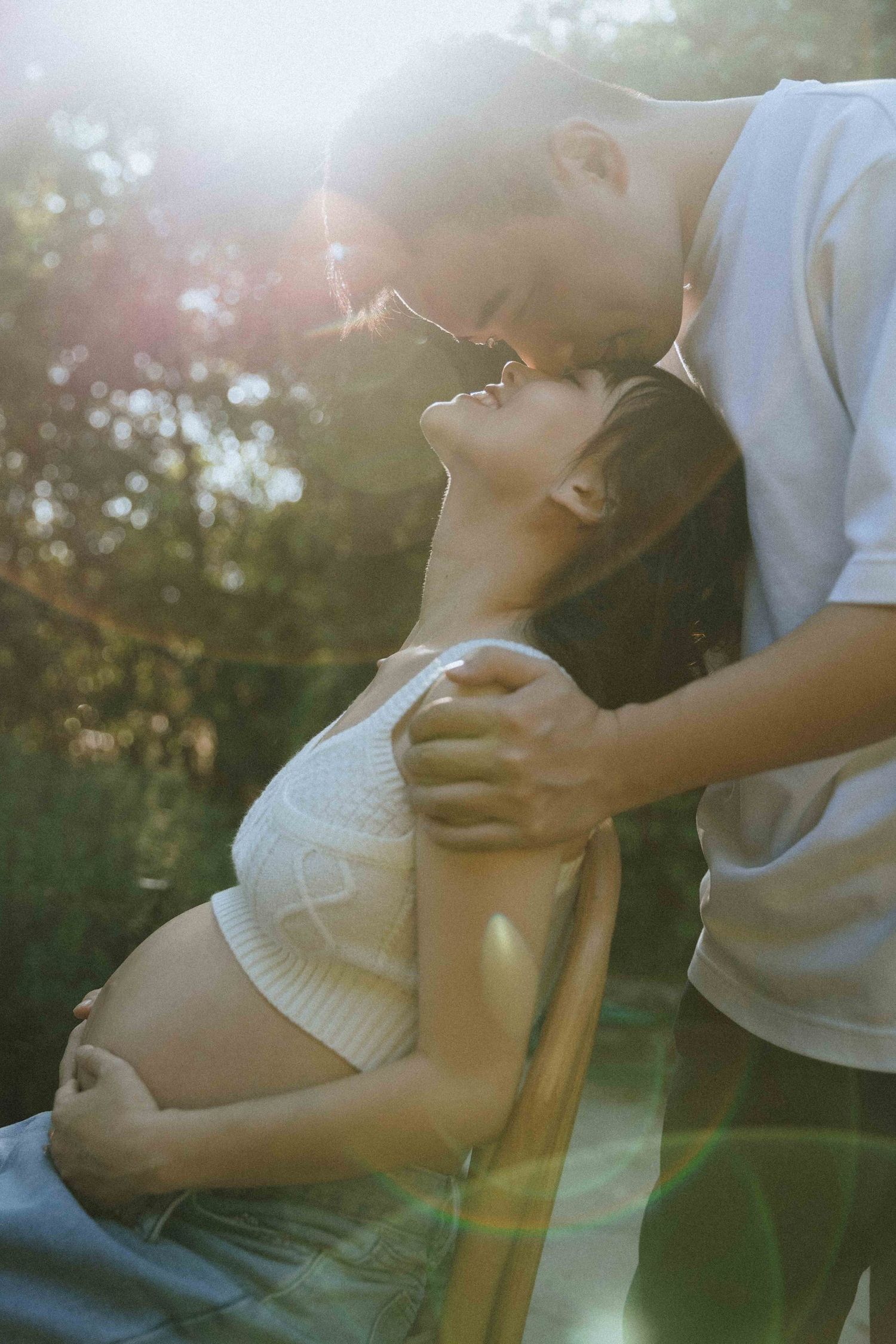 Intimate maternity moments captured in warm sunlight with couple on wooden chair.
