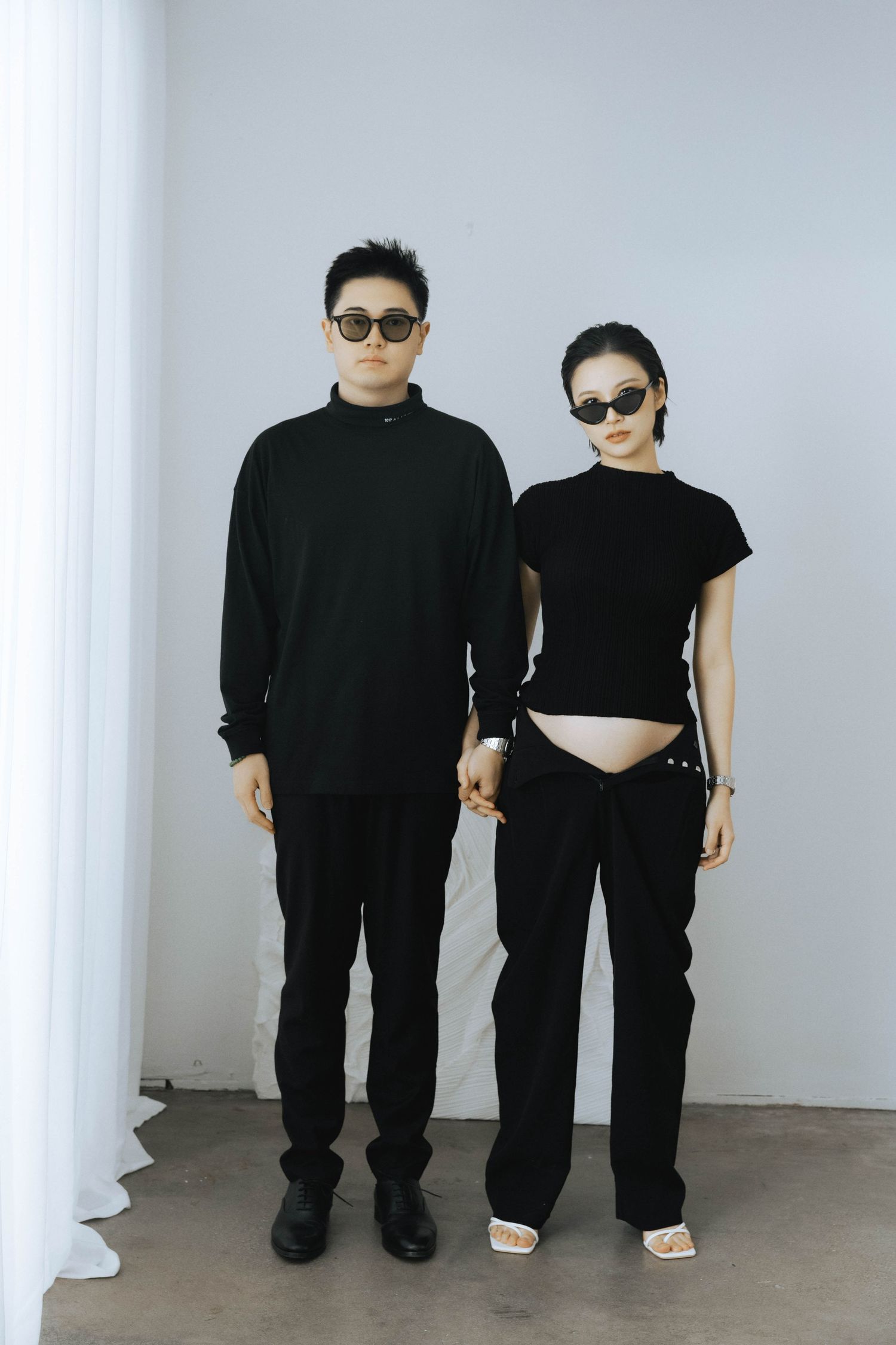 Artistic black and white studio portraits of couple in matching dark outfits.