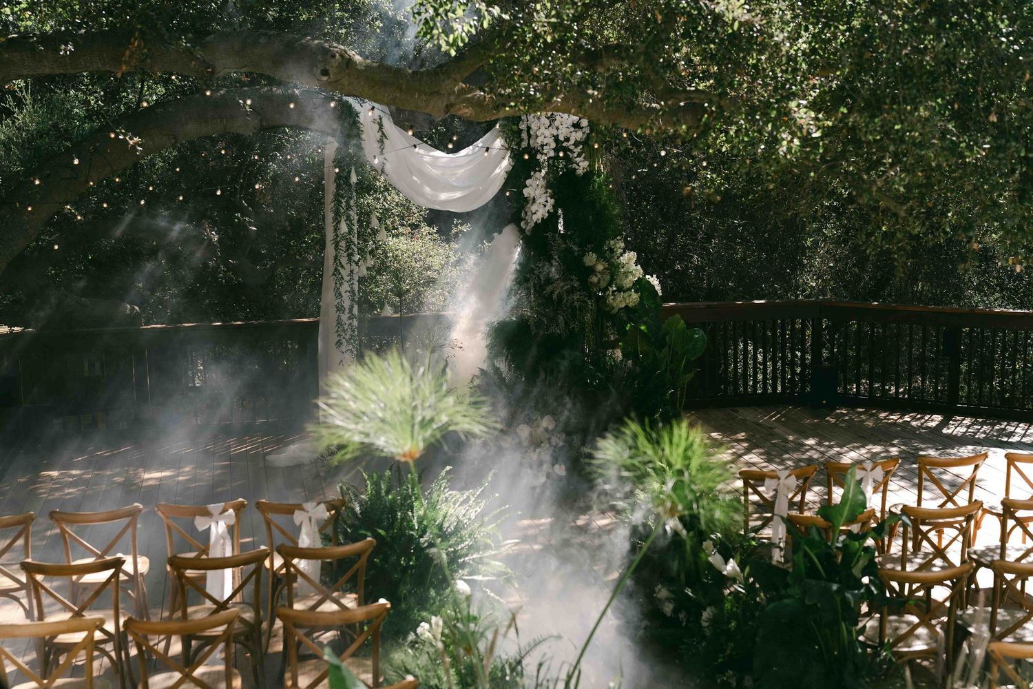 Garden wedding venue with ethereal white draping and natural mist among trees.