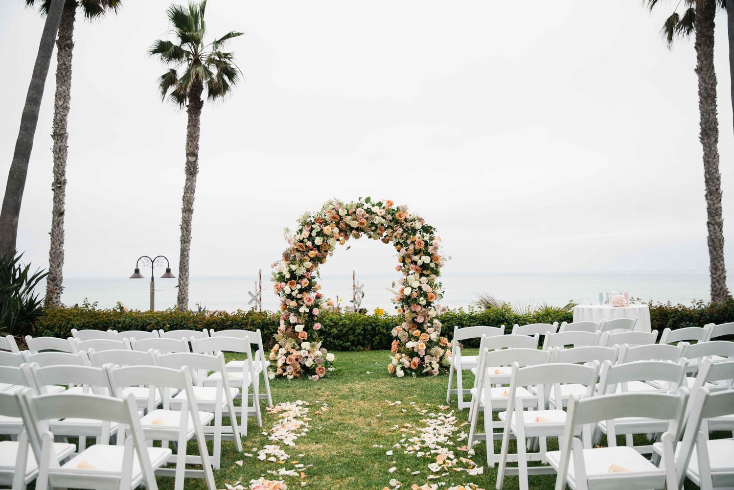 Wedding ceremony site with white chairs and floral-decorated arches against a coastal backdrop.