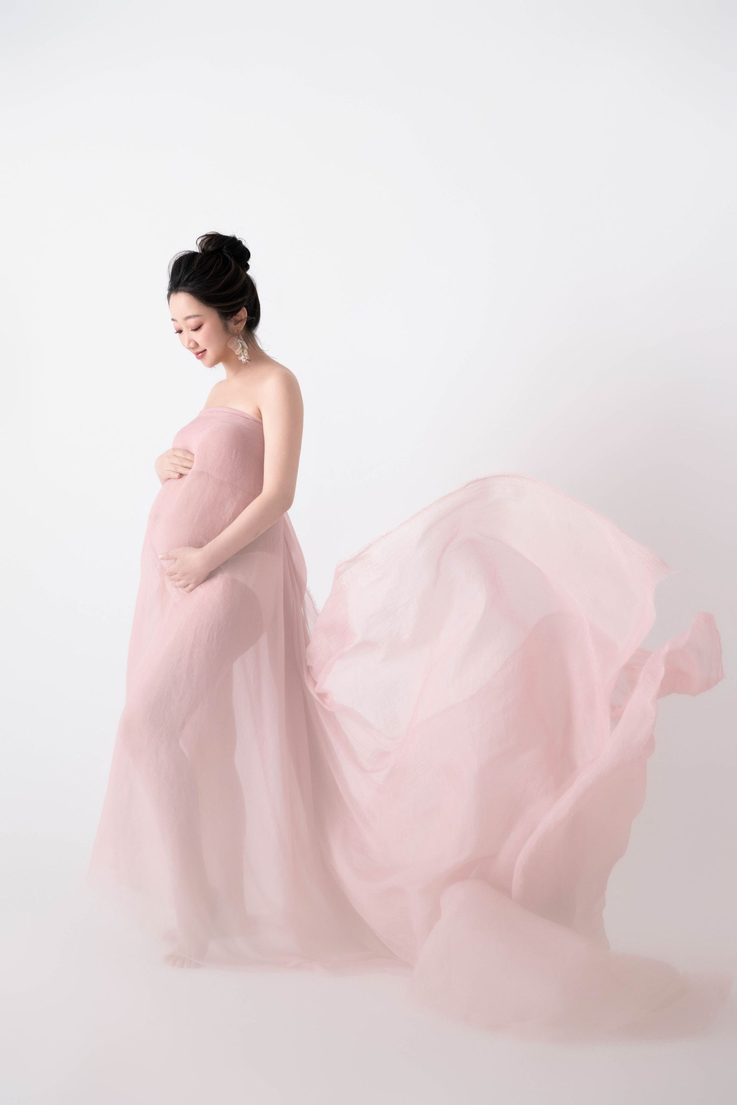 Dreamy maternity portraits with floating pink chiffon fabric in studio.