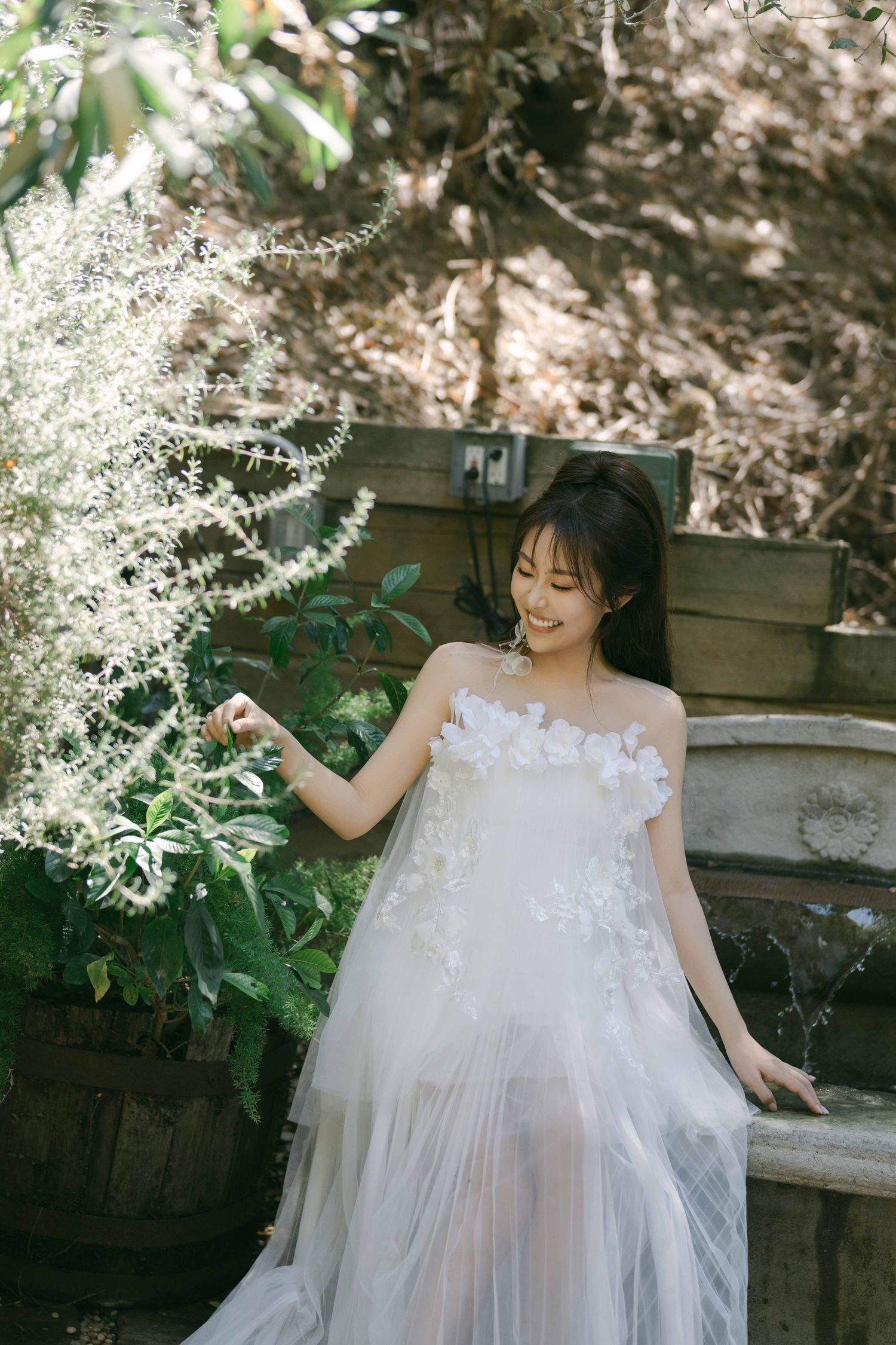 Ethereal white wedding dress with floral details photographed in a garden setting.