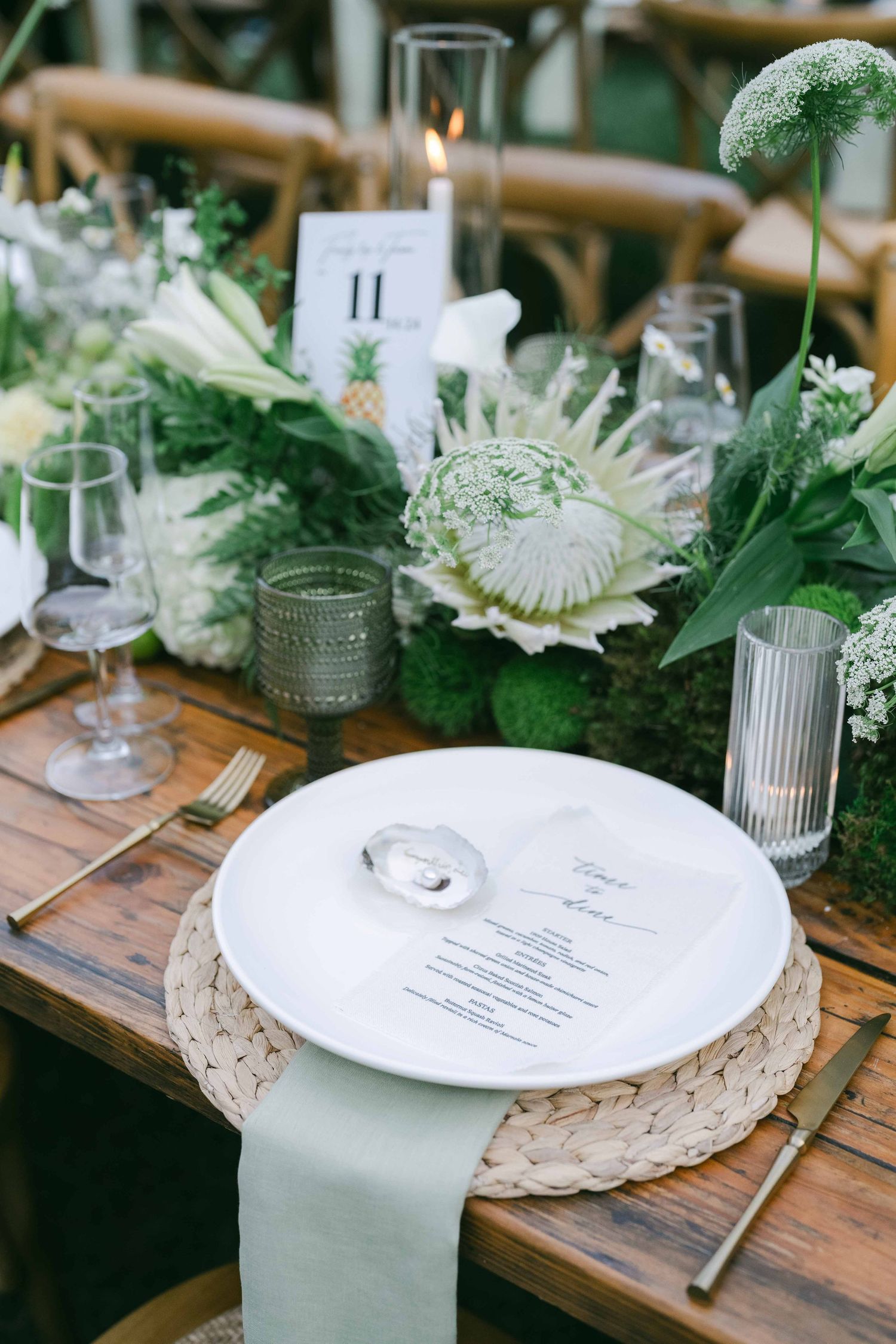 Elegant table setting with woven placemats, white plates, and greenery on wooden tables.