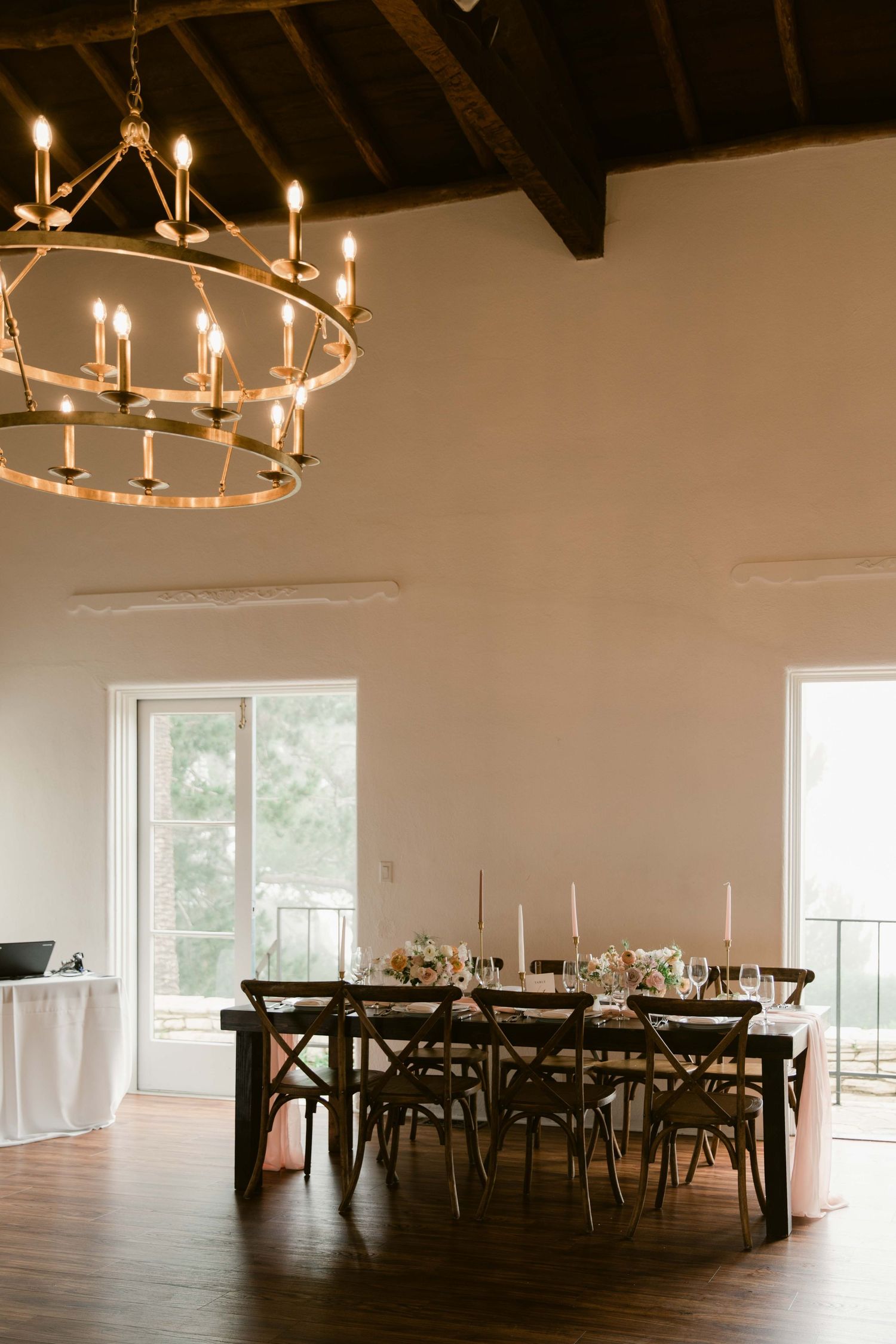 Modern dining room with circular chandelier, wooden tables and high vaulted ceilings with exposed beams.
