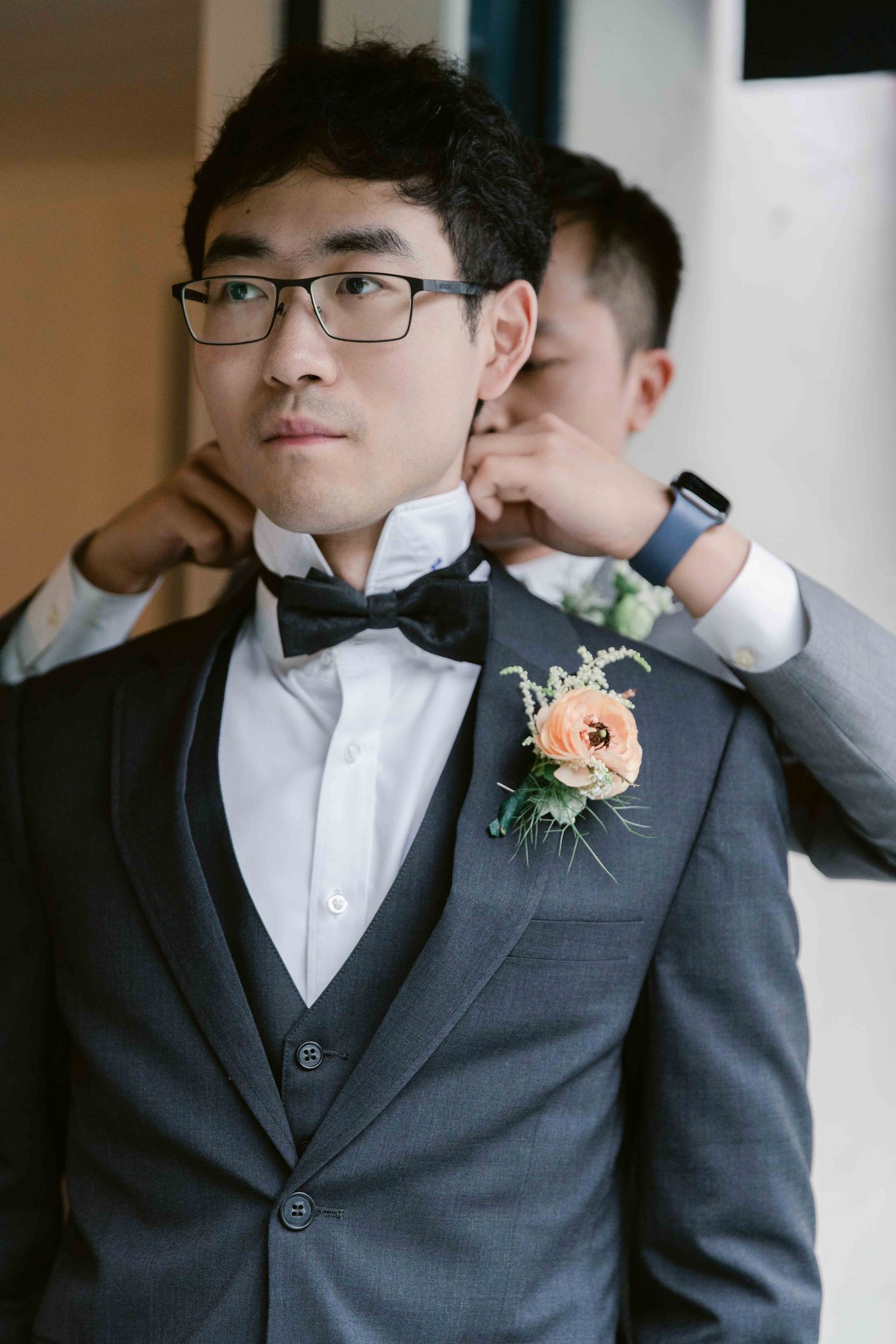 Formal portrait of groomsman wearing grey suit with peach boutonniere and bow tie.