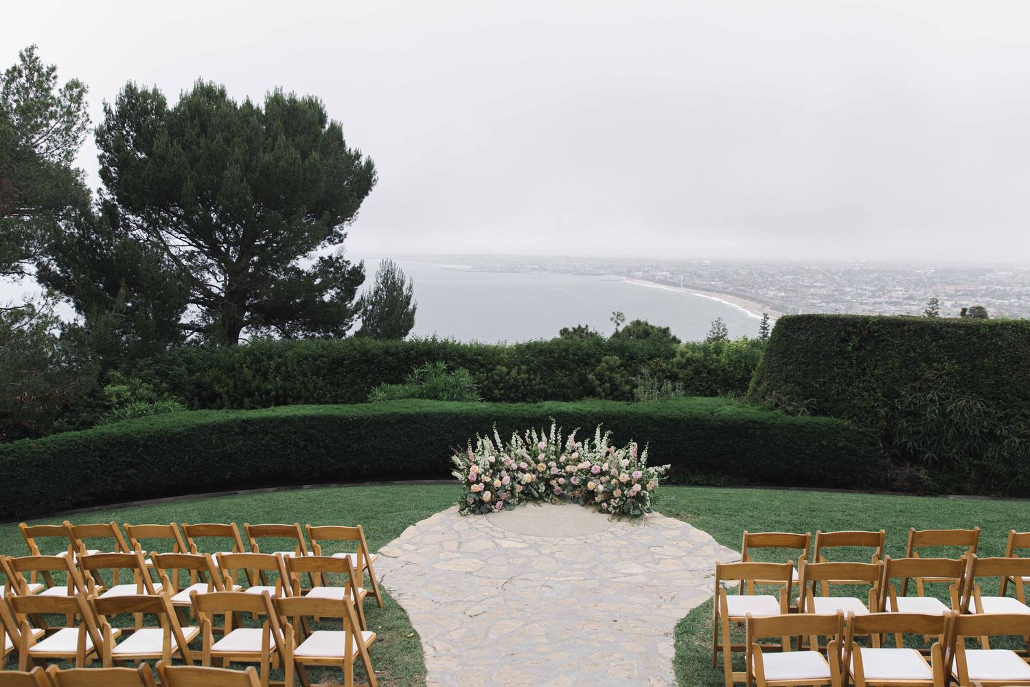Outdoor wedding ceremony setup with wooden chairs and floral arch overlooking a scenic view.