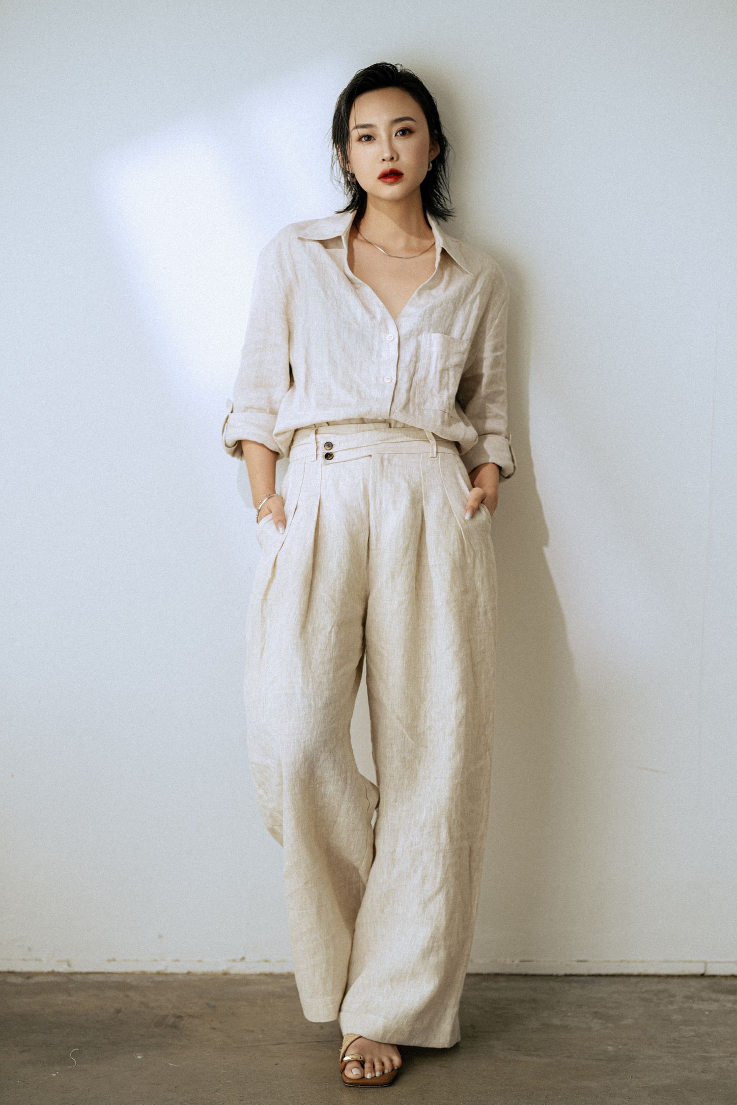 Wide-leg linen jumpsuit styled with casual elegance against minimalist backdrop.