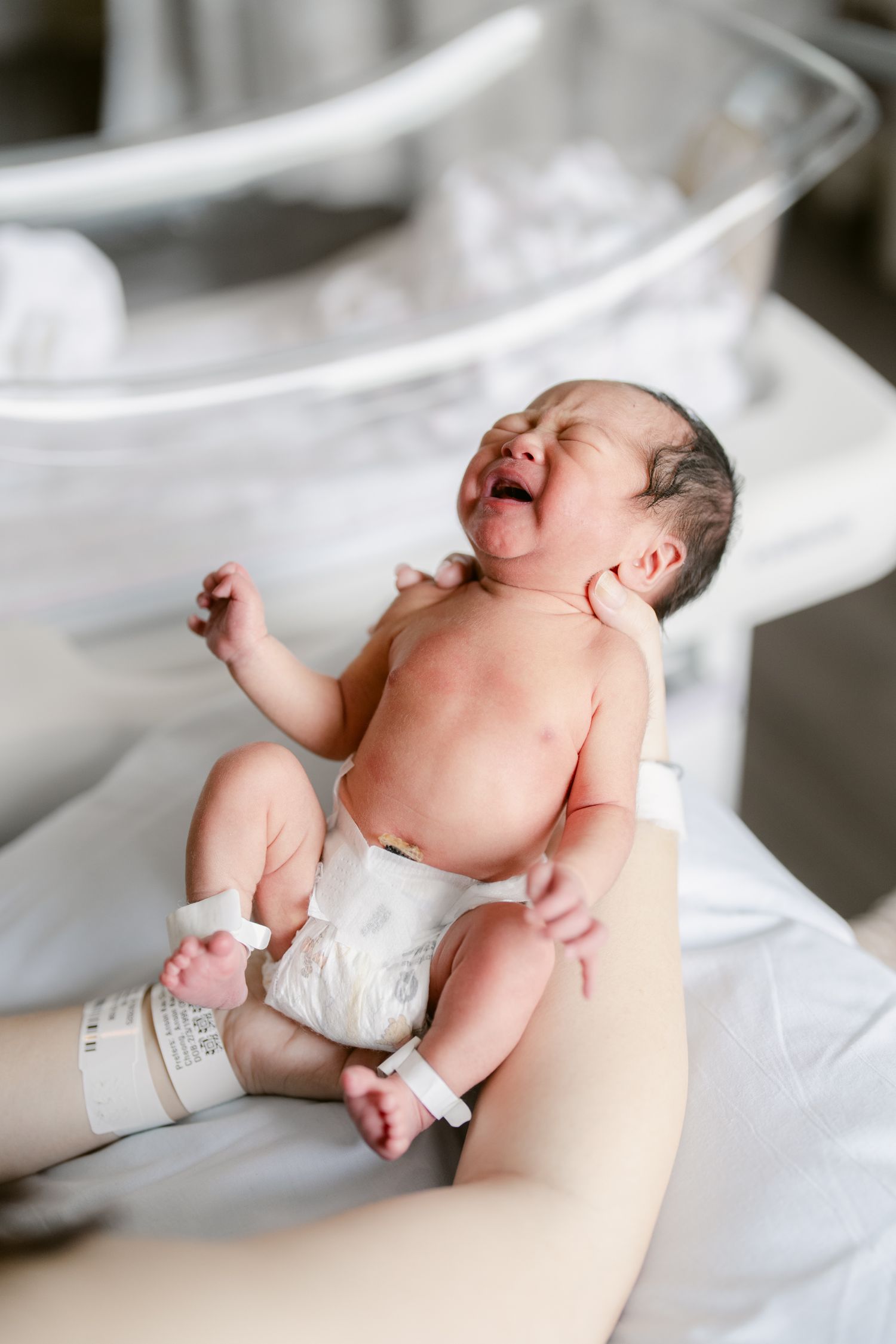 Newborn baby stretching and yawning while lying on white bedding.
