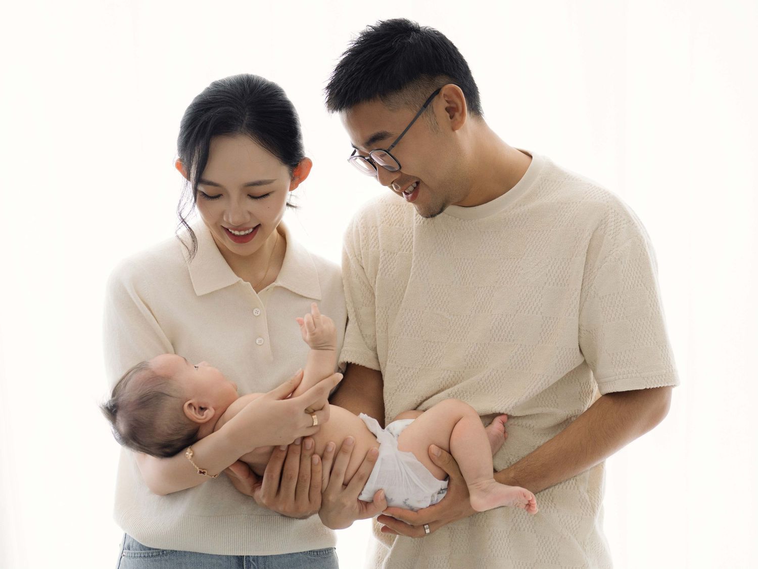 Parents cuddling with baby in casual white and beige outfits.