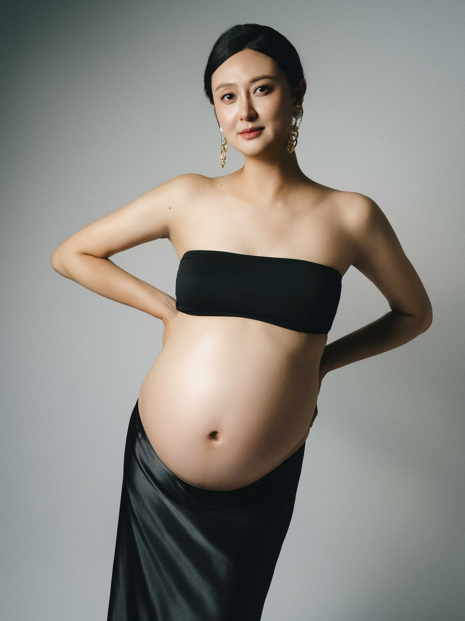 Modern maternity photography with black fabric draping over pregnant belly.