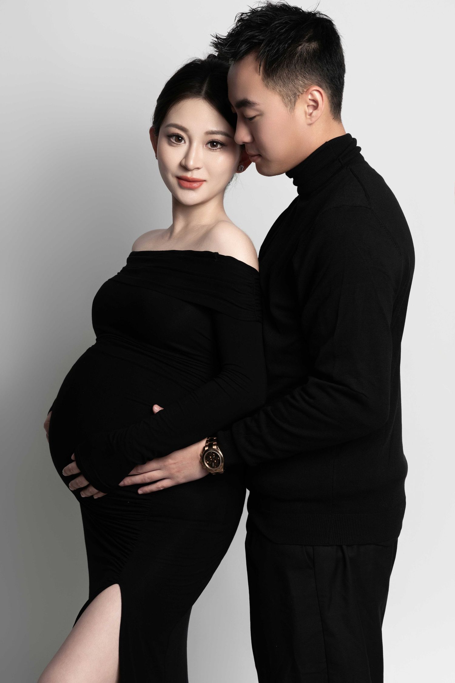 Intimate maternity photoshoot featuring a couple in black attire against white background.