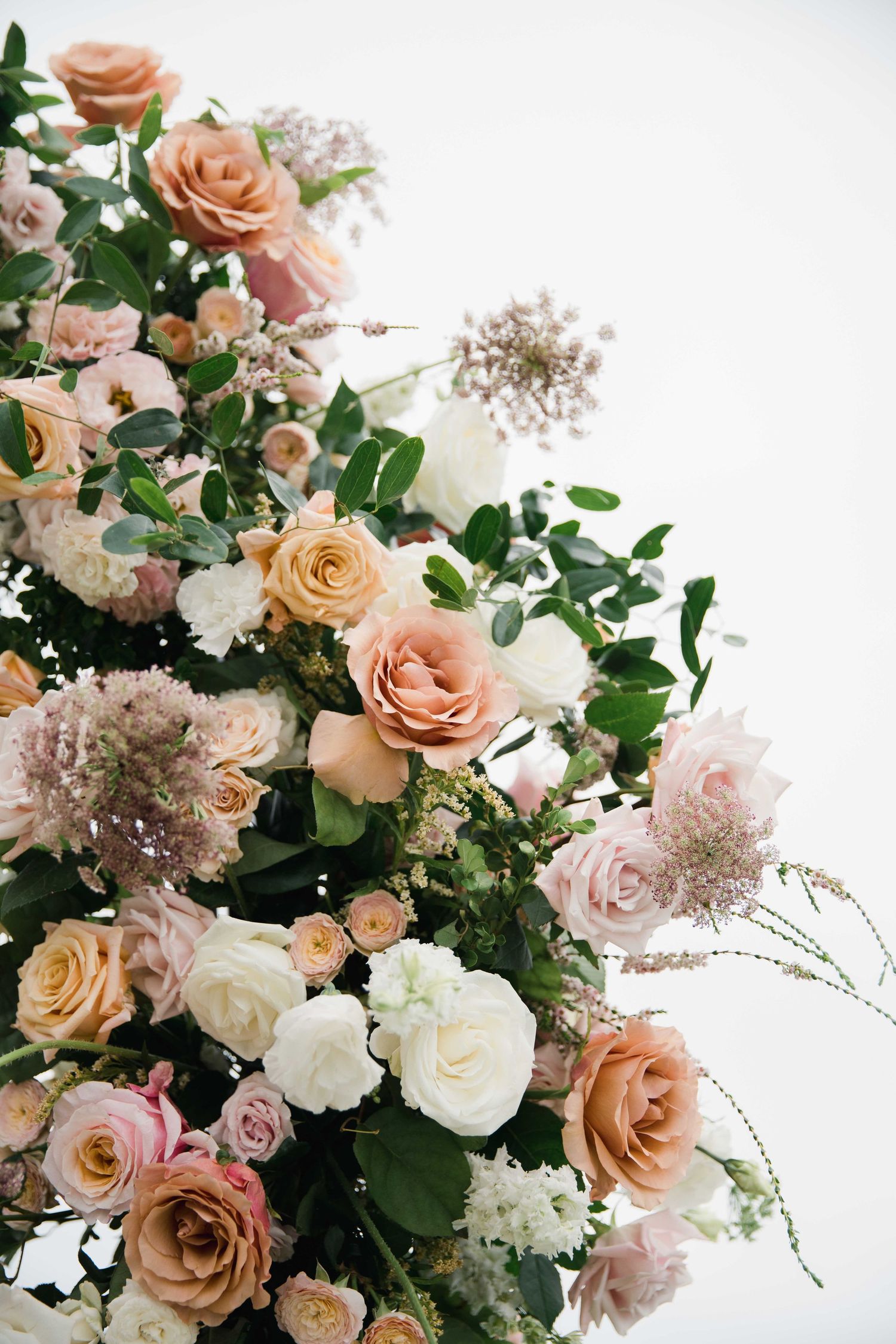 Lush floral arrangement featuring peach roses, white flowers, and green foliage.