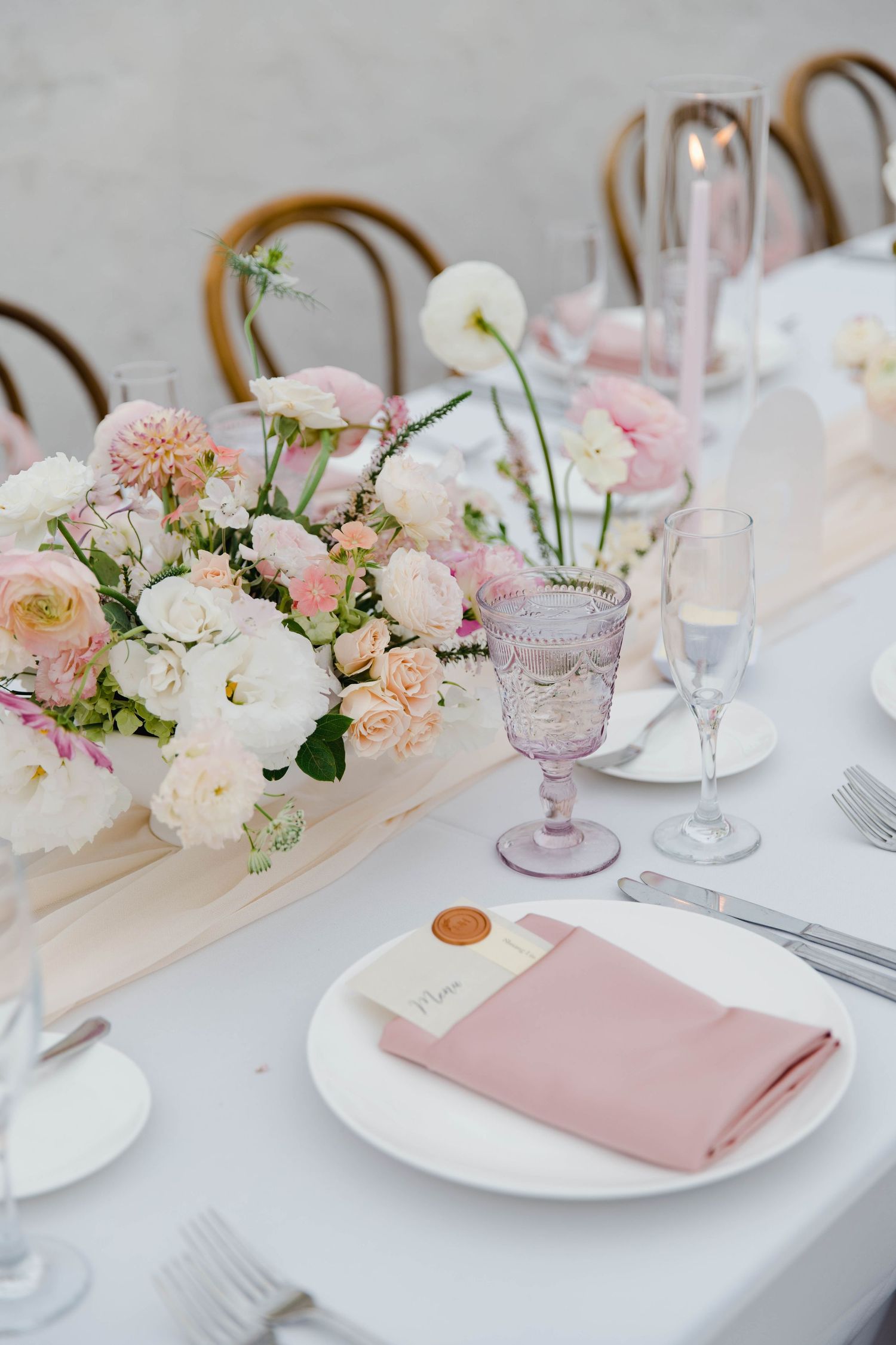 Wedding table settings with pink and white floral centerpieces and blush napkins.