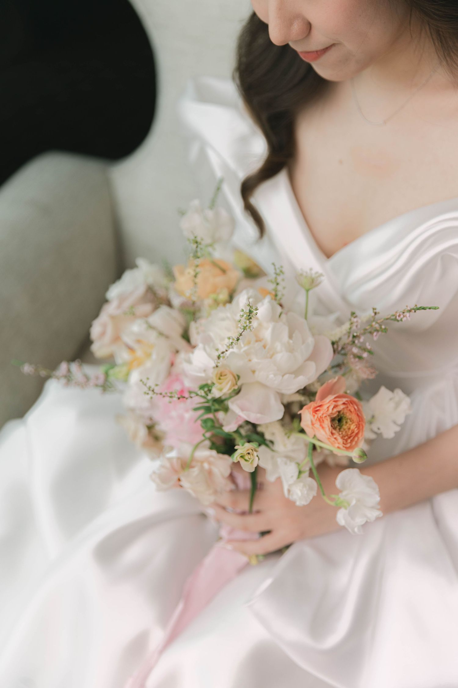 Close-up of pastel bouquet with coral and pink flowers against white bridal gown.