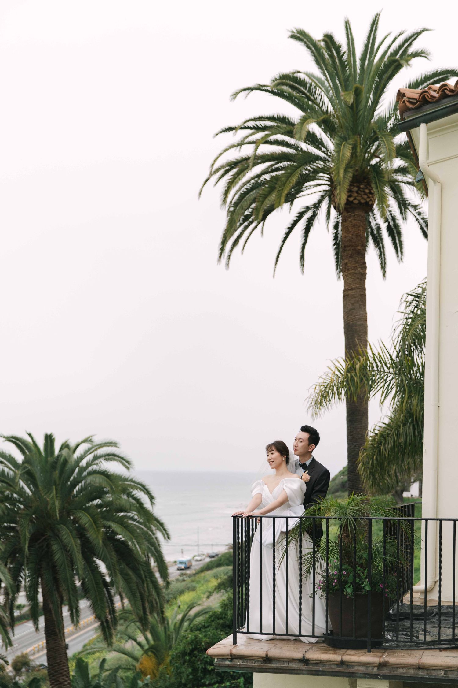 A couple enjoys a romantic moment on a balcony overlooking palm trees and ocean views.