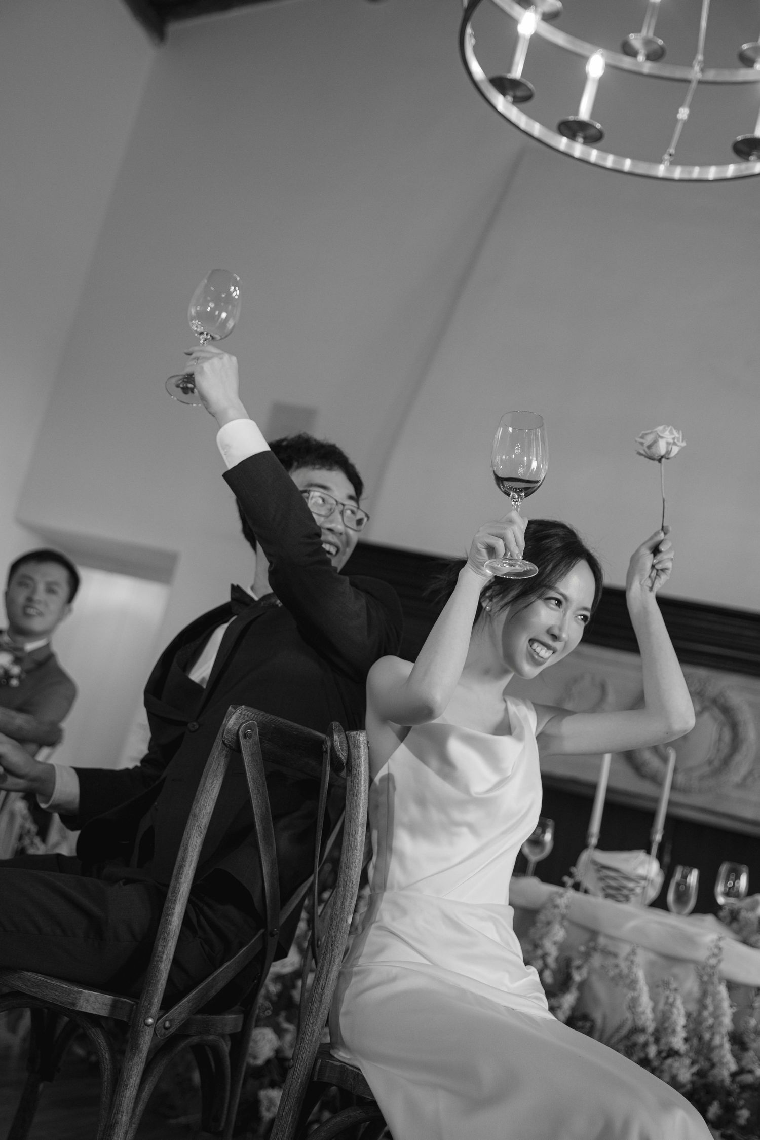Wedding guests raise their glasses in celebration during a joyful toast at an indoor reception.