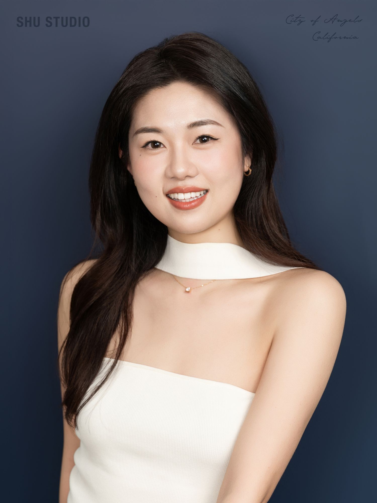 Elegant portrait in white strapless top against dark navy studio background.