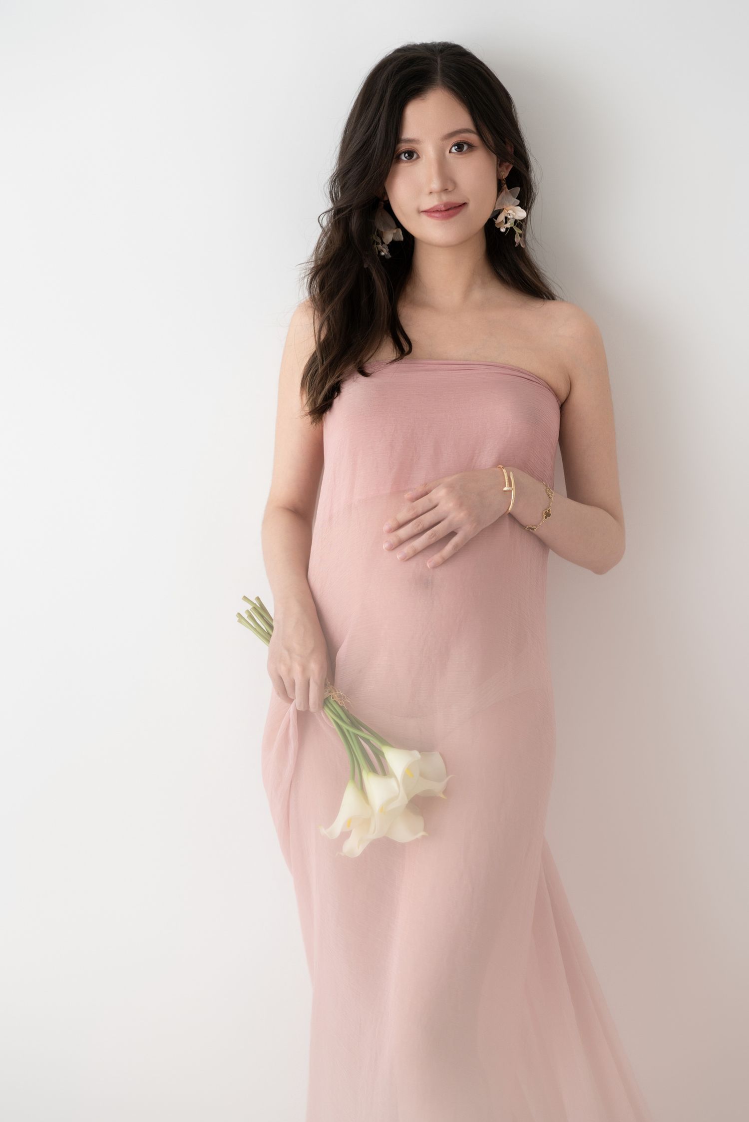 Elegant maternity portrait series in soft pink dress with white background.