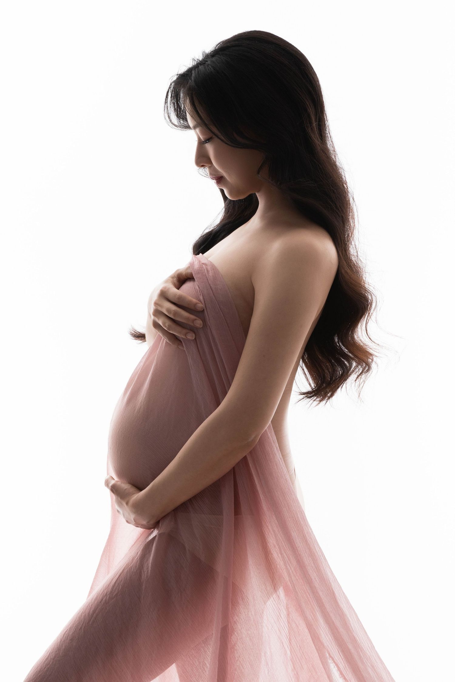 Romantic maternity photos with flowing pink fabric in soft lighting.