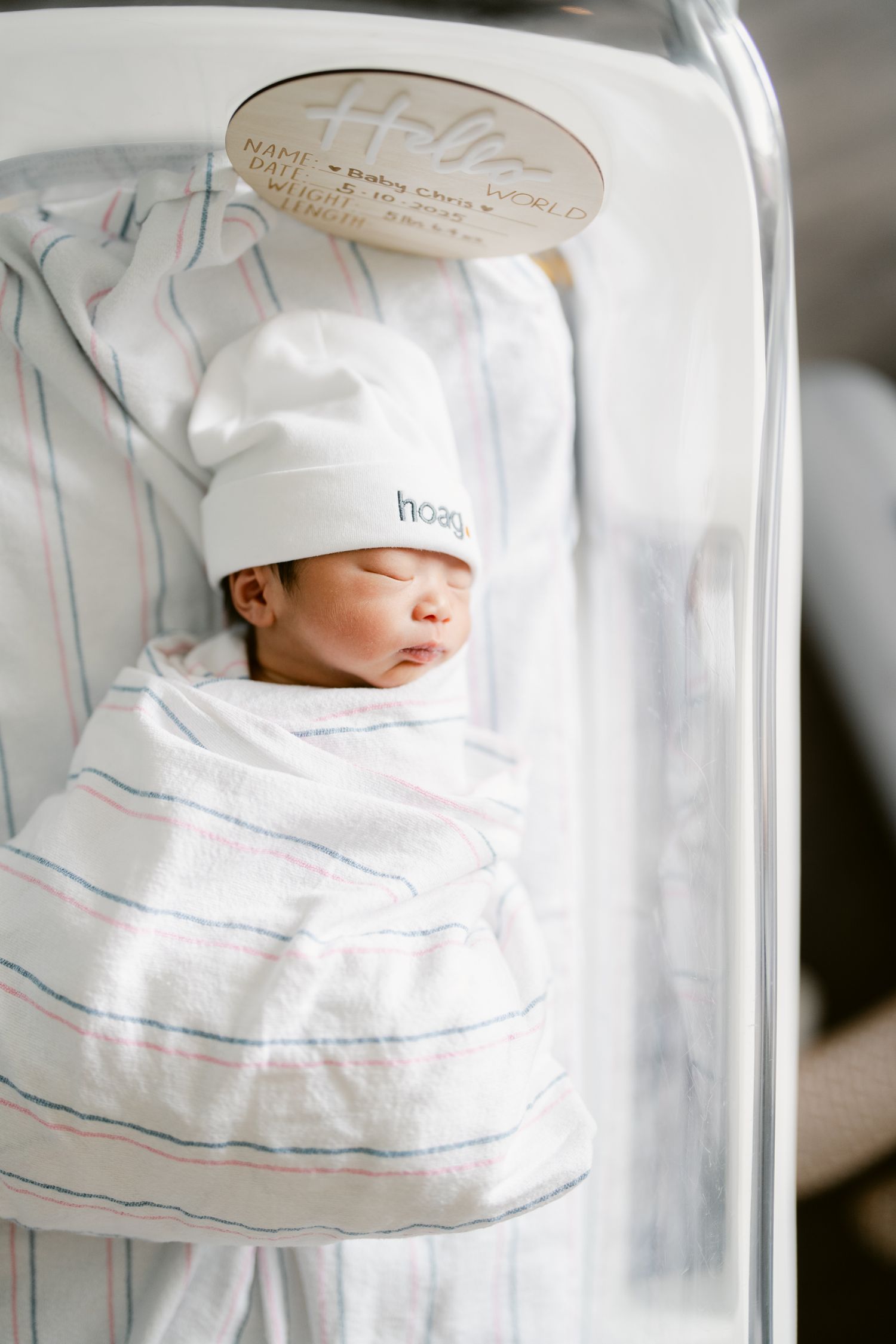 Newborn baby wrapped in white and blue striped hospital blanket resting peacefully.