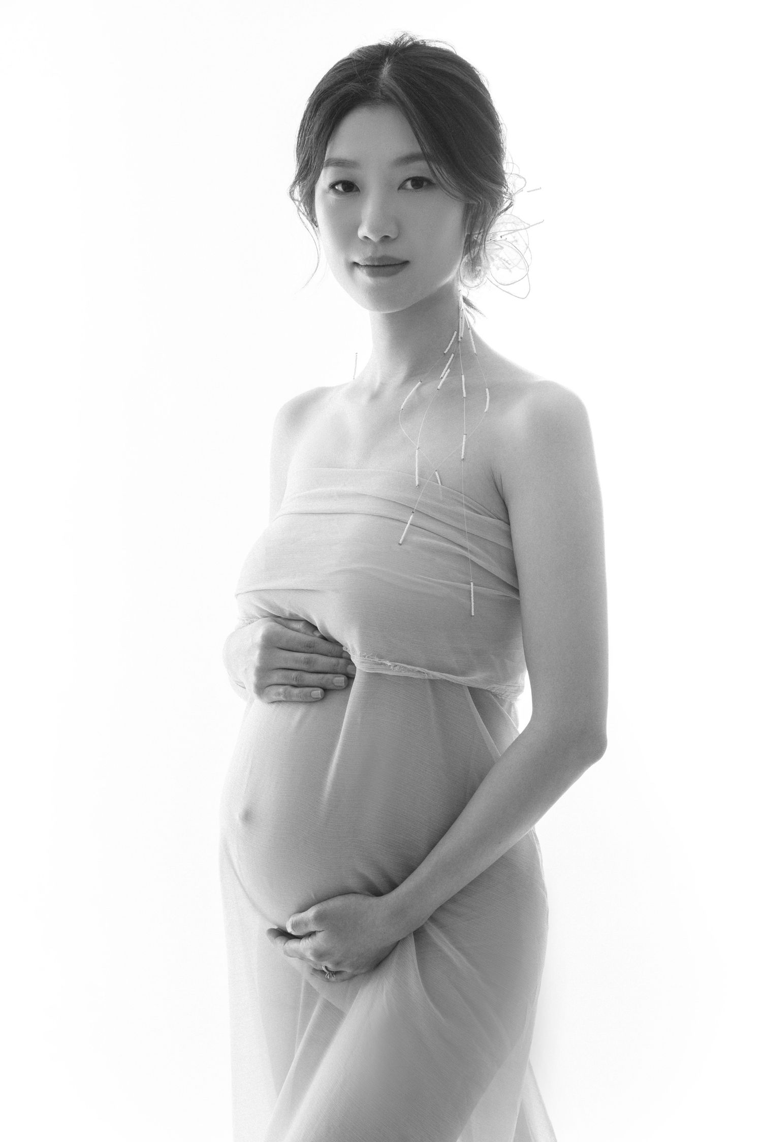 High-key maternity portrait series with soft white fabric draping.