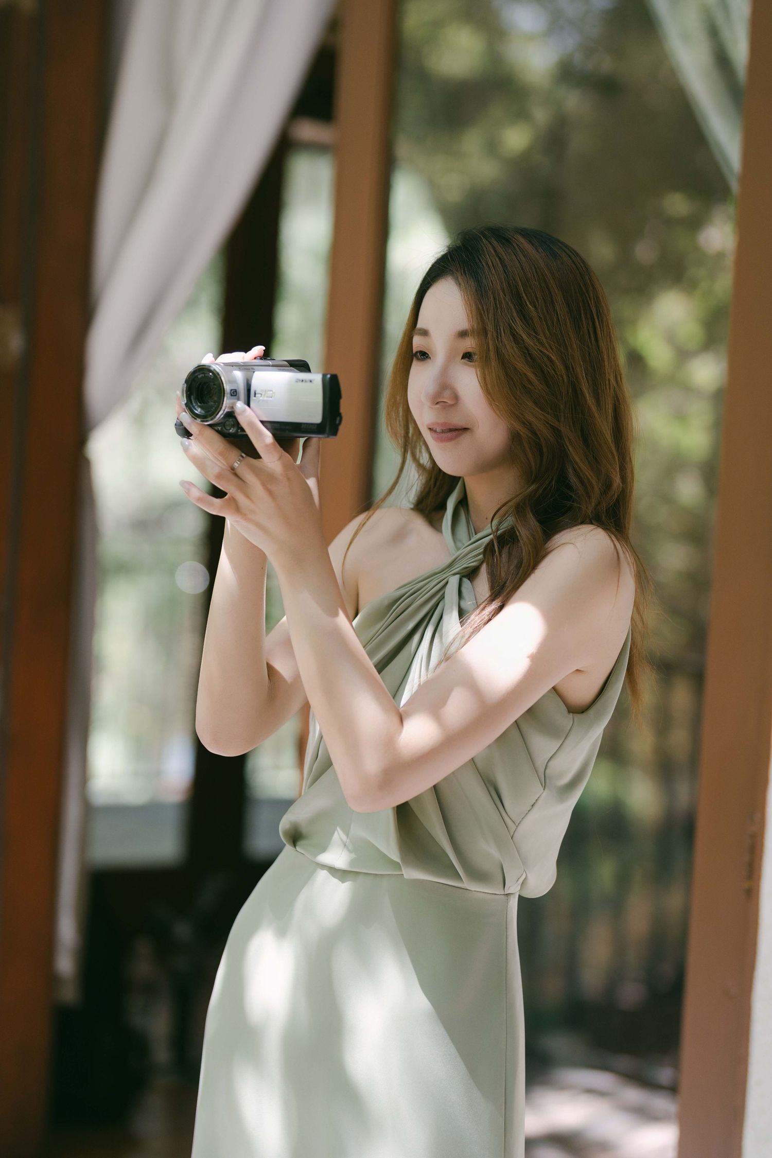 Photographer in light colored dress capturing moments in natural window light.