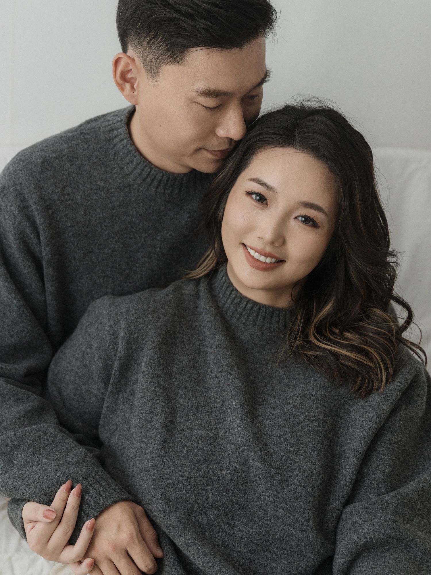 Couple in matching sweaters sharing intimate moment on light background.