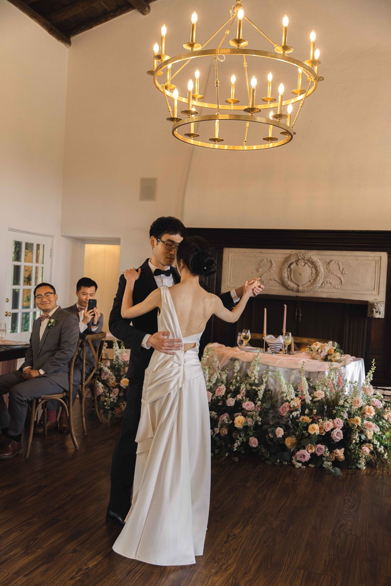 Wedding reception dance floor with circular chandeliers and floral decorations.