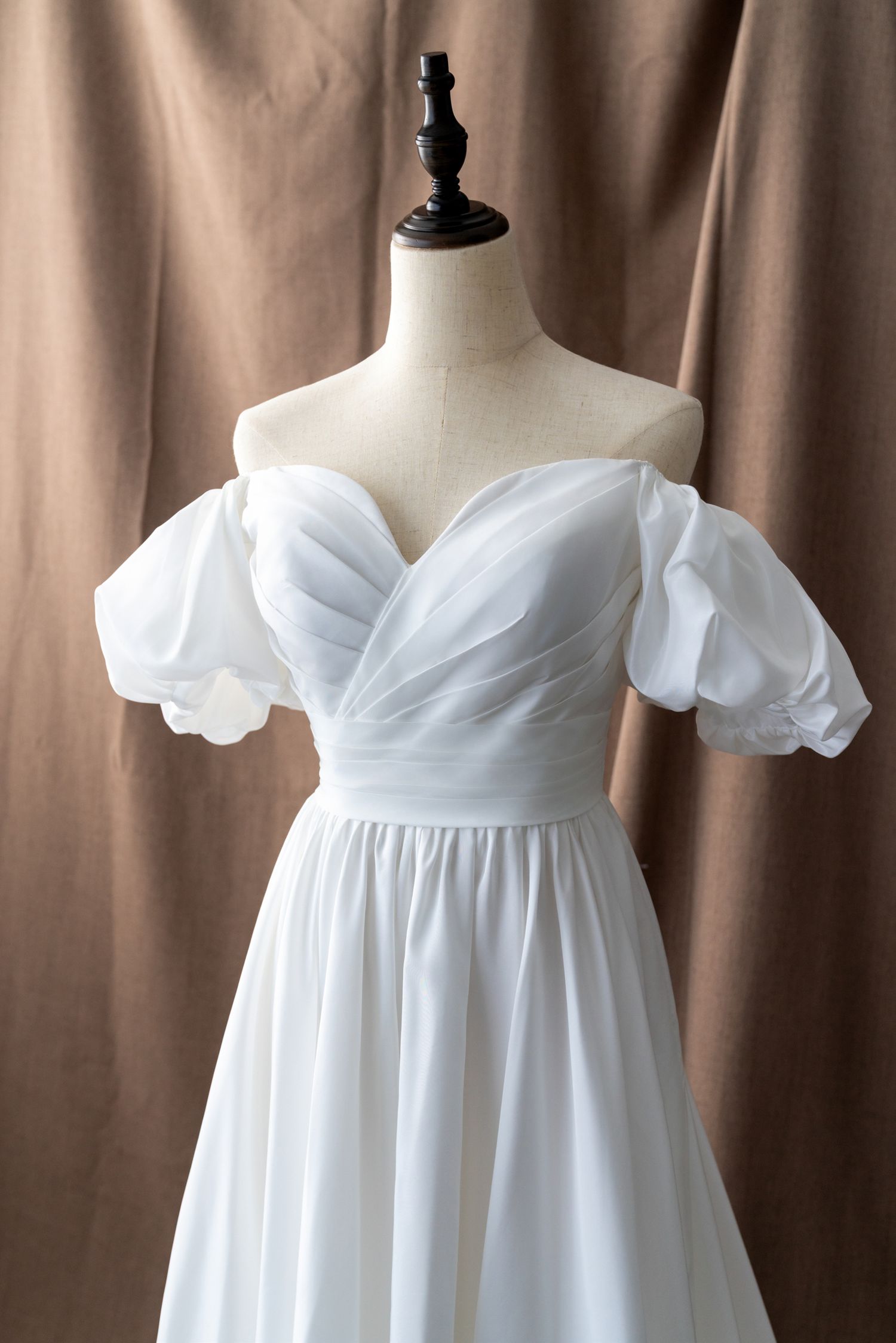 Off-shoulder wedding dress with puff sleeves and sweetheart neckline shown on display form.