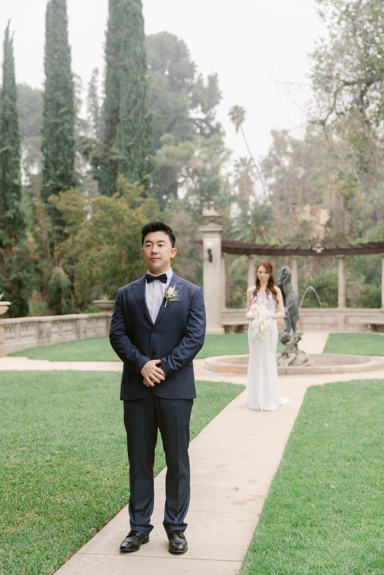 A wedding couple shares a special moment on a path lined with cypress trees.