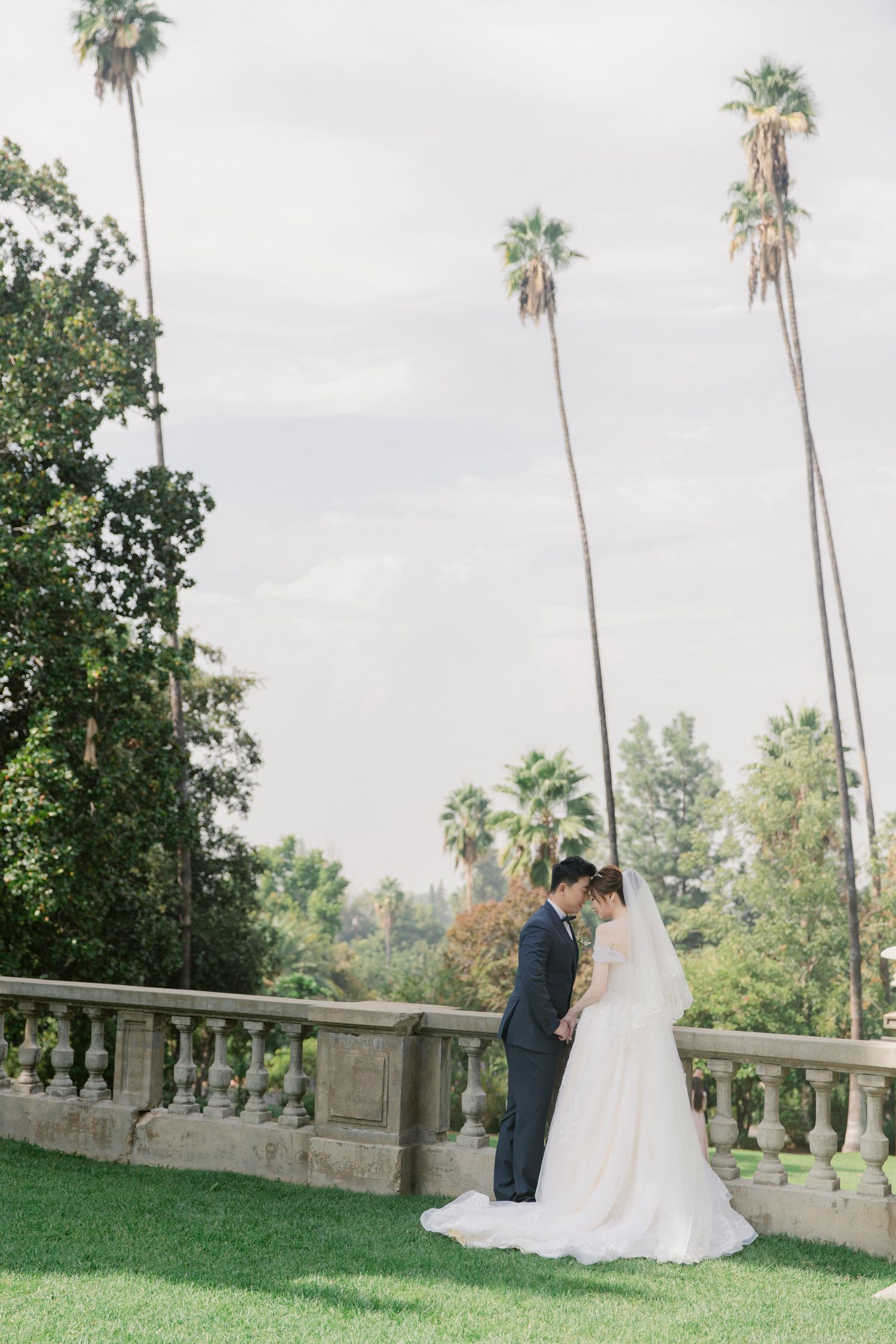 Romantic wedding couple moment captured on stone terrace with palm trees in background.