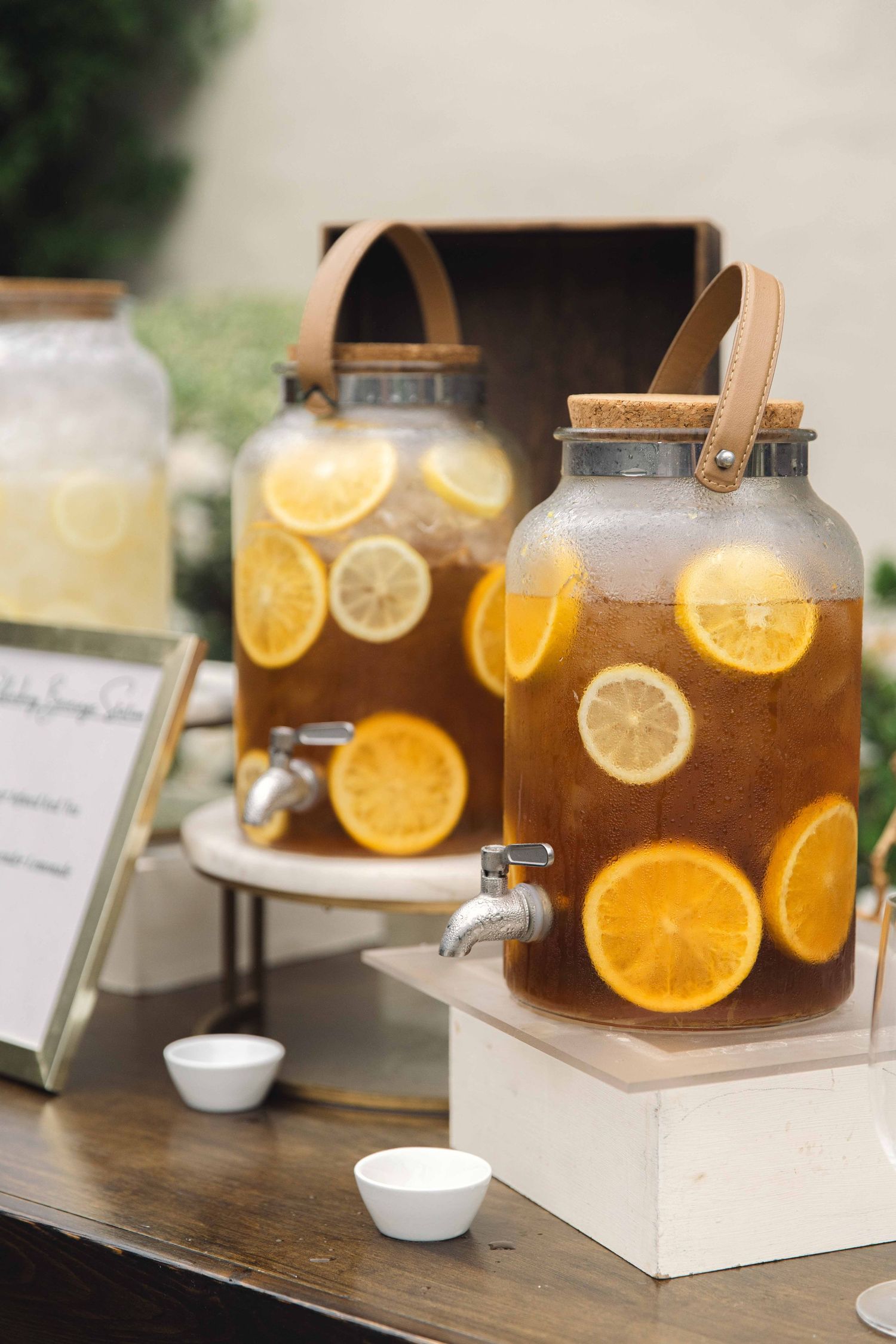 Beverage dispensers filled with citrus-infused drinks on wooden display stands at outdoor event.