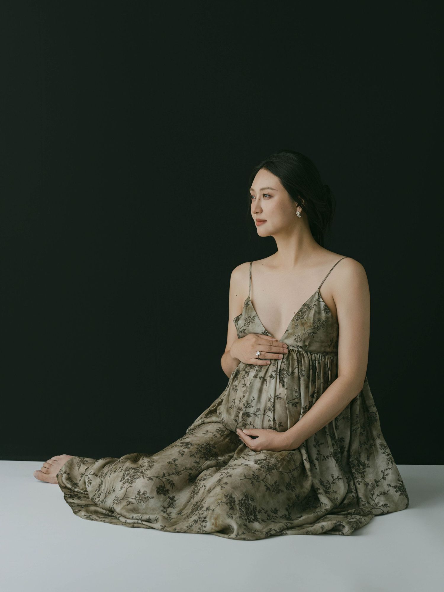 Elegant maternity poses with flowing grey dress against dark studio backdrop.