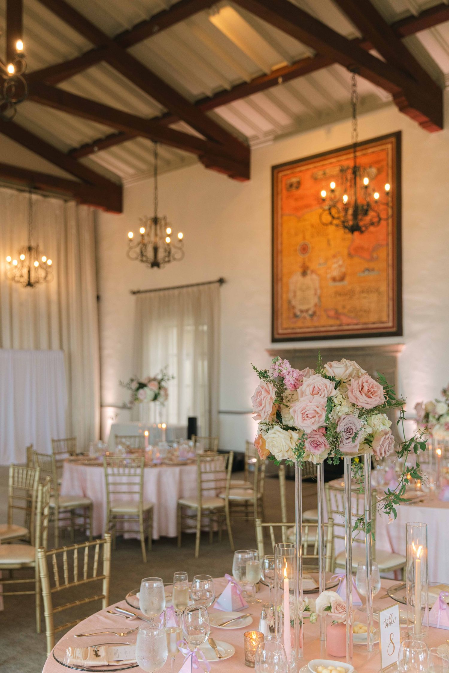 Rustic wedding reception venue with exposed beams, chandeliers and elegant table settings.