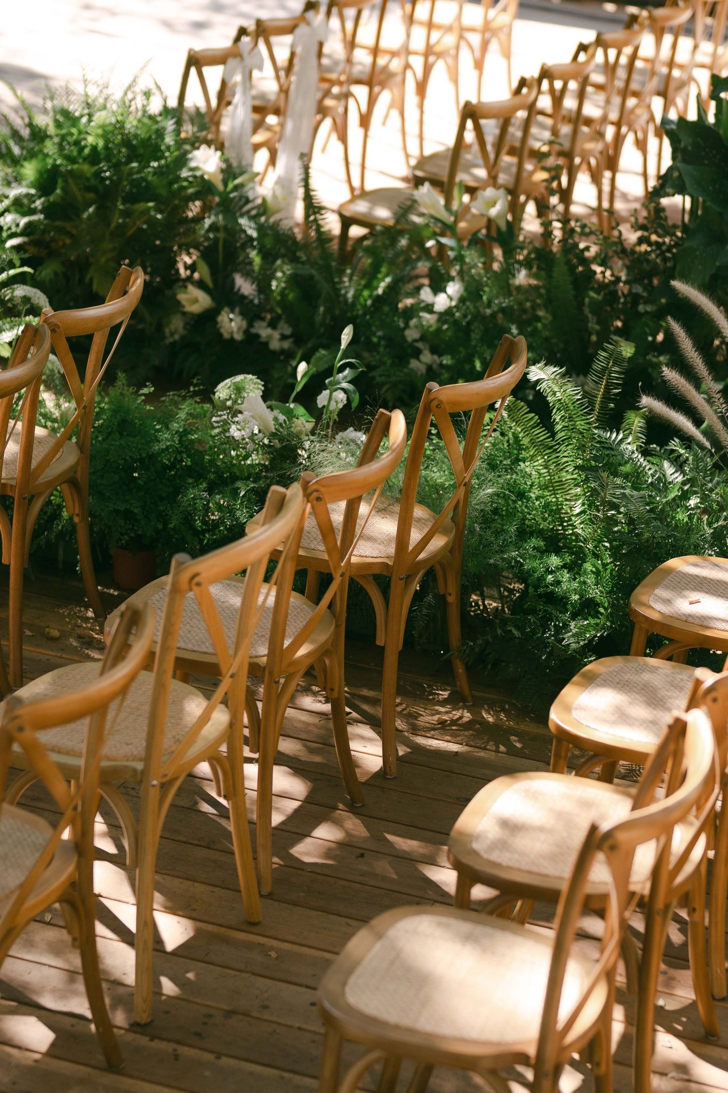 Wooden crossback chairs arranged in rows for an outdoor wedding ceremony.
