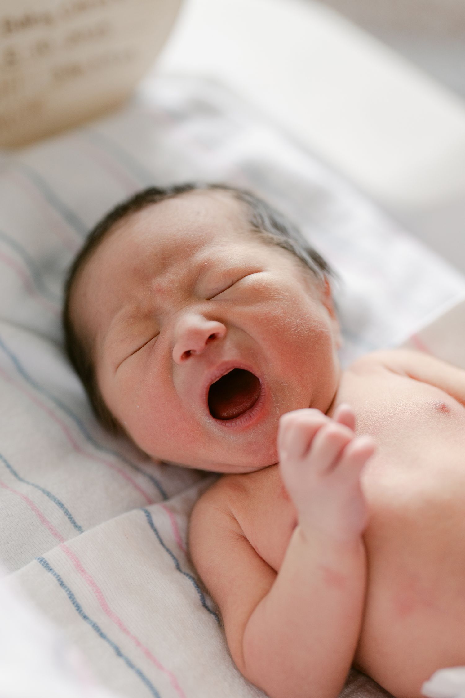 Newborn baby sleeping peacefully on hospital bedding with blue stripes.