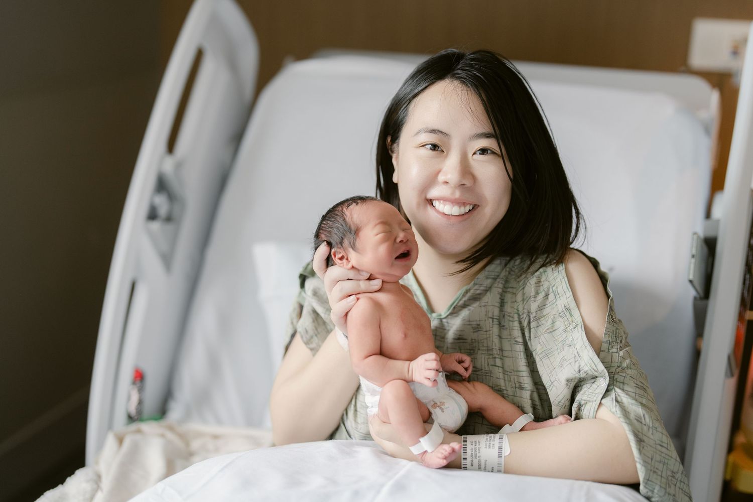 A newborn baby lies in a hospital bassinet while receiving care from medical staff.