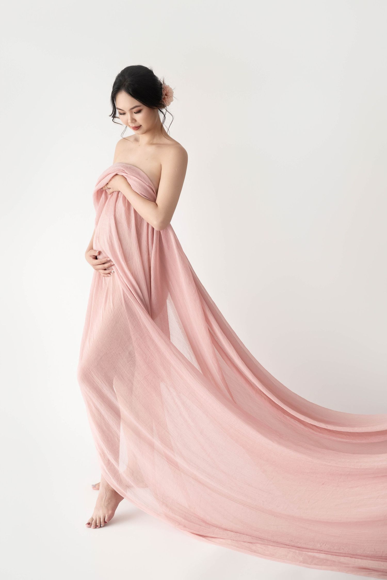 Artistic maternity photo featuring flowing pink fabric in minimalist studio.