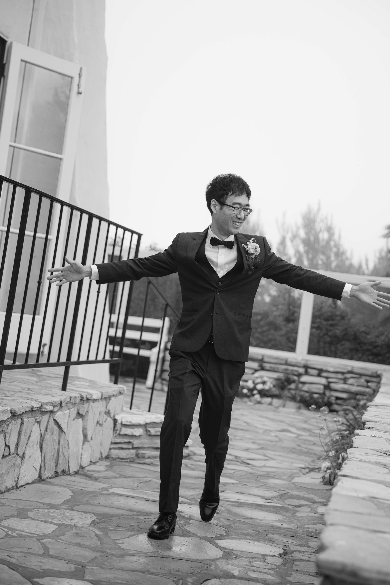 A person in formal attire strikes playful poses on a stone patio during a wedding photoshoot.