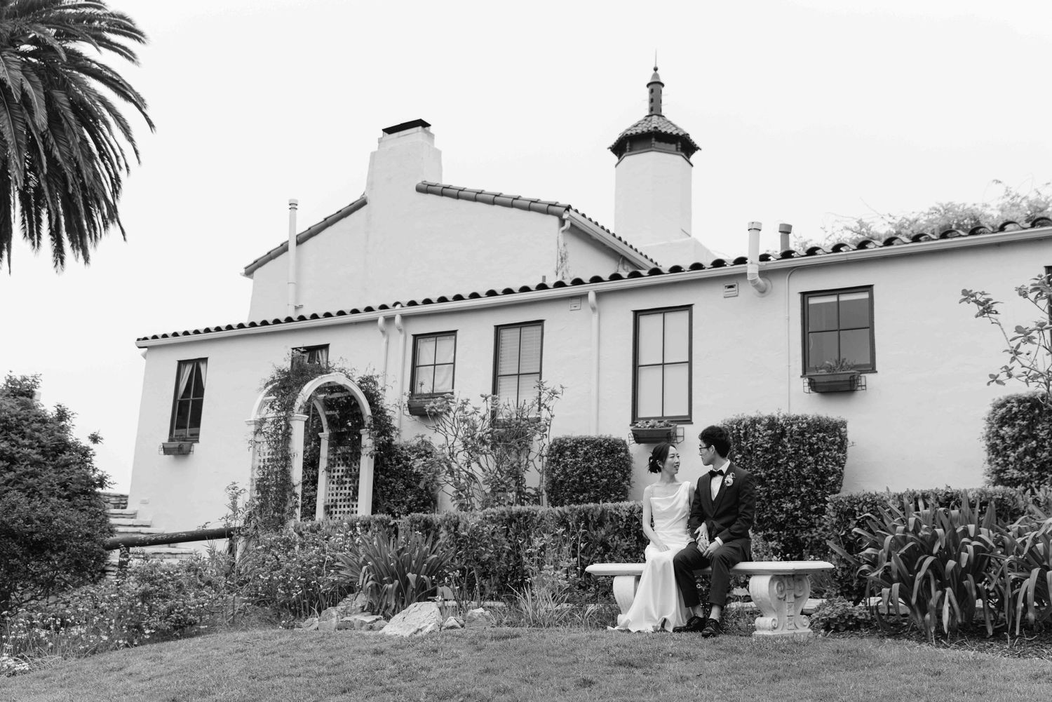 Black and white photo of a Spanish colonial style house with palm trees and garden.