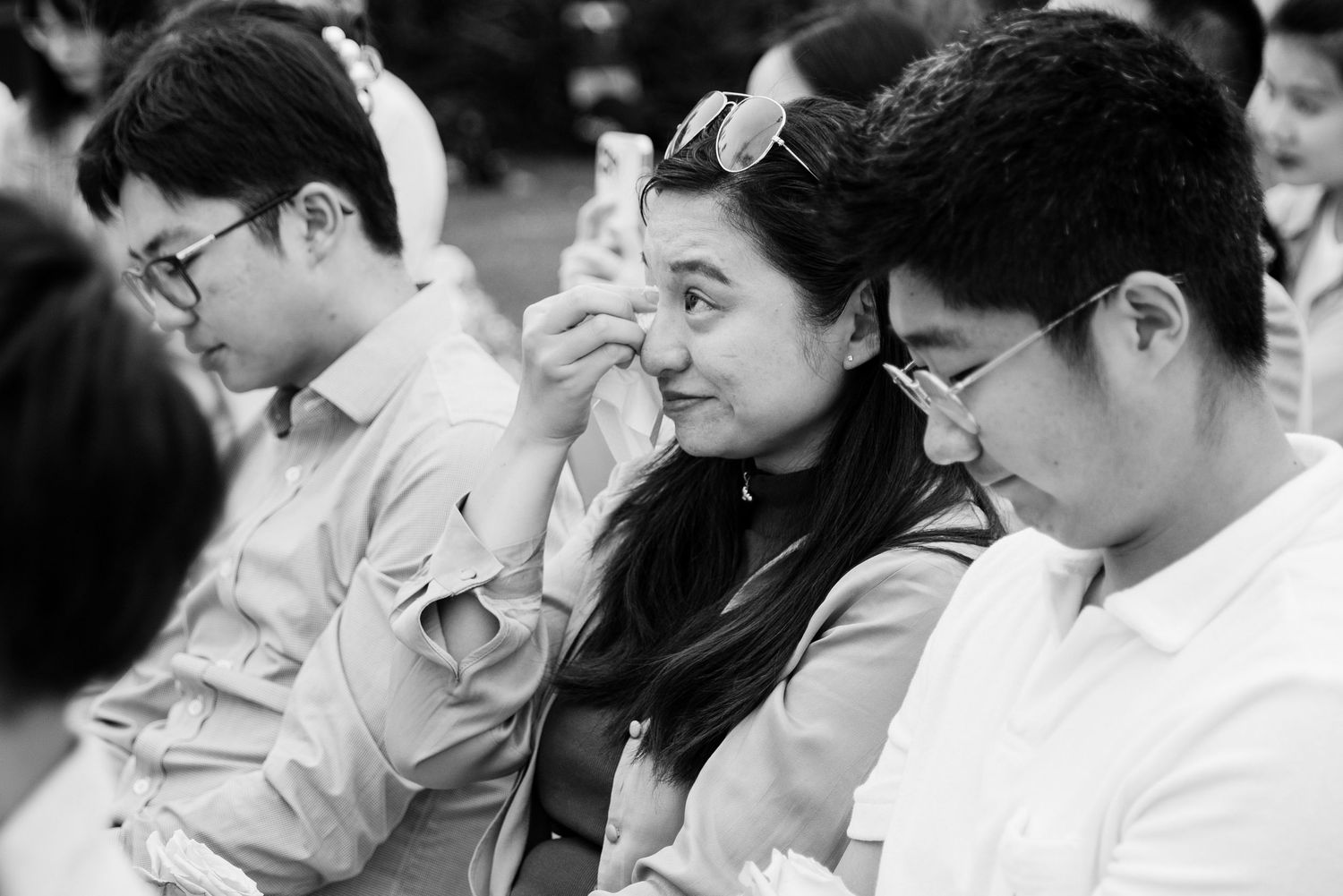 Black and white candid shot of wedding guests sitting together during ceremony.