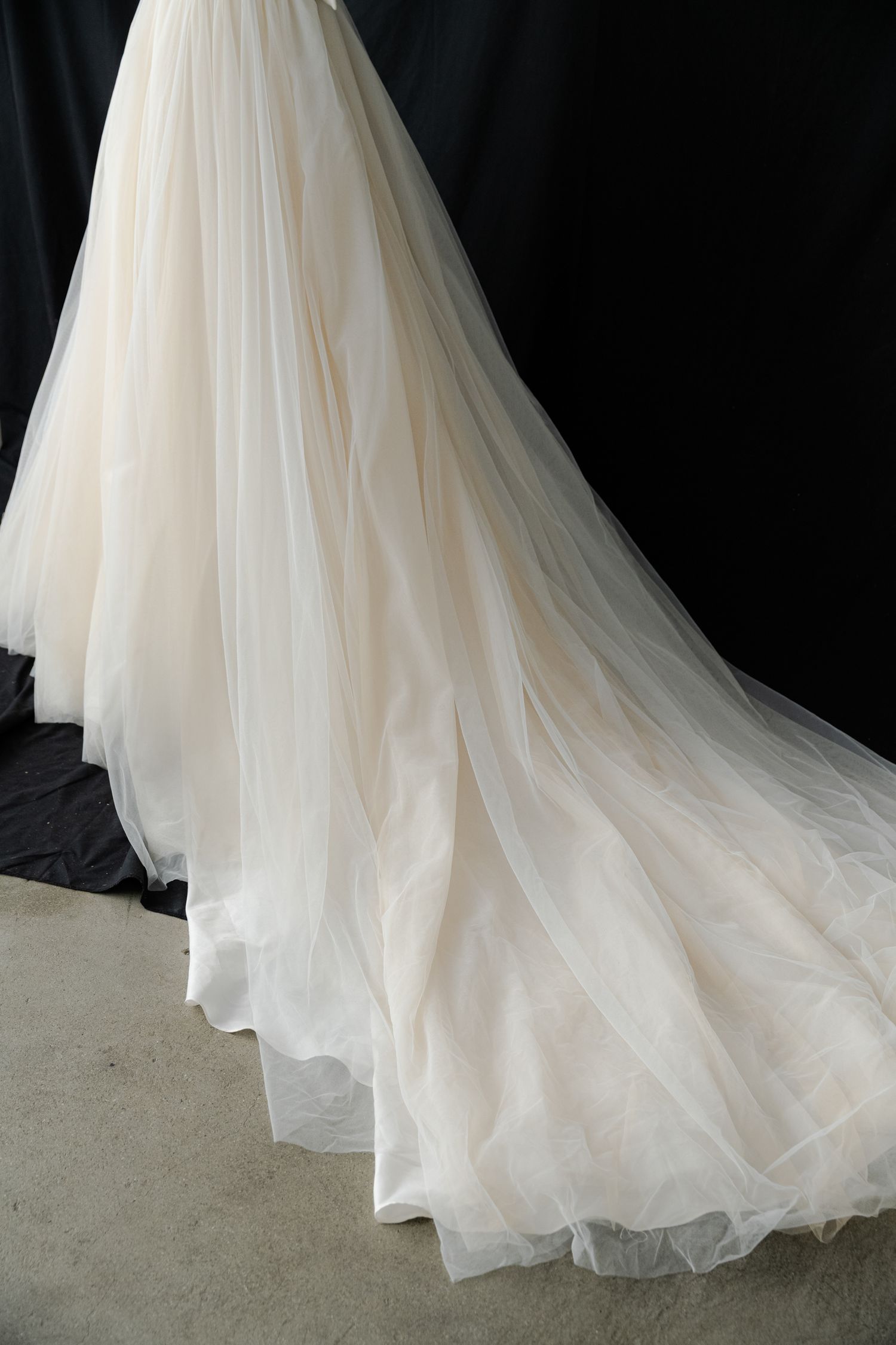 Flowing white tulle wedding dress train photographed against black background.