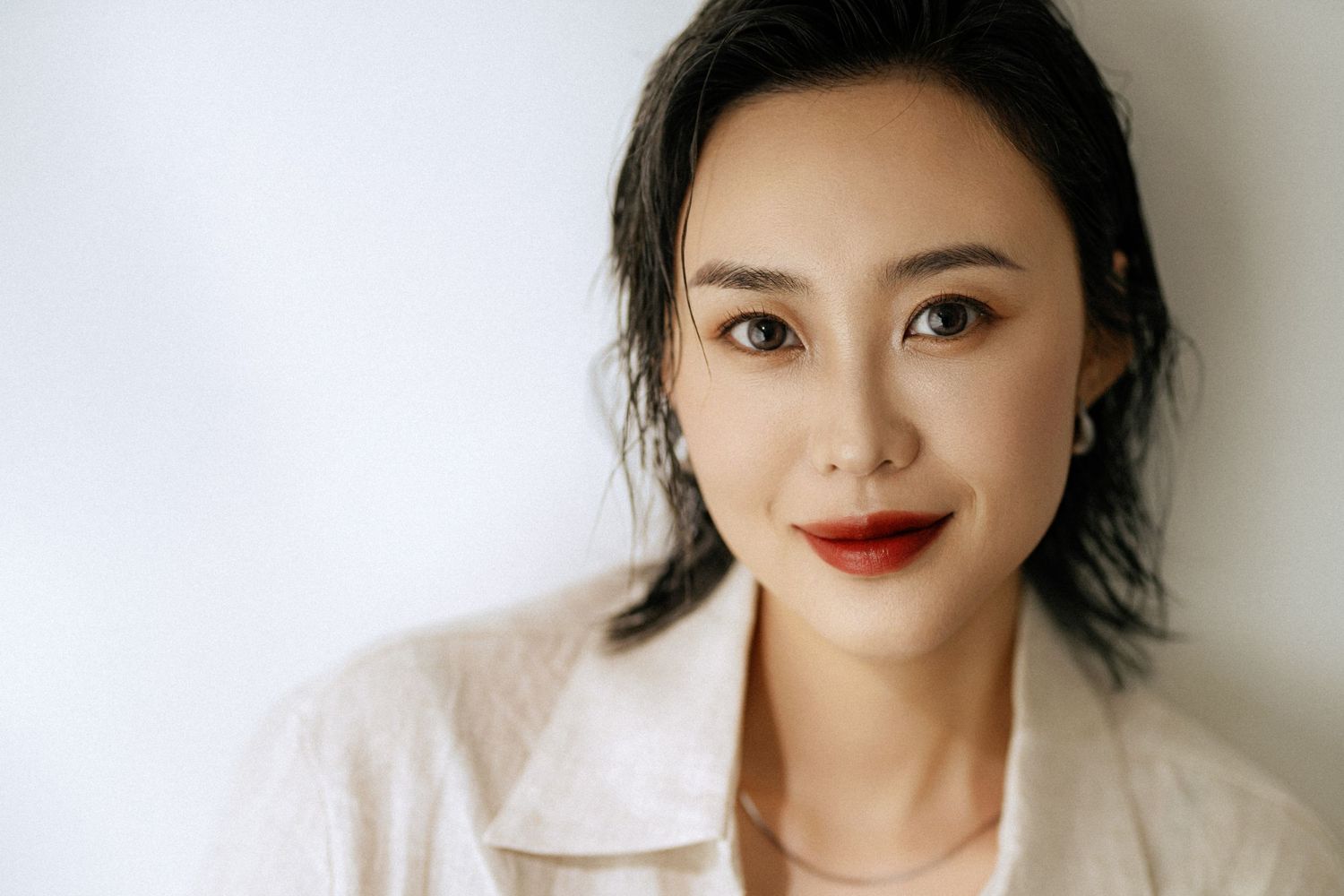 Clean beauty portrait with classic red lip and soft makeup look in light colored jacket.