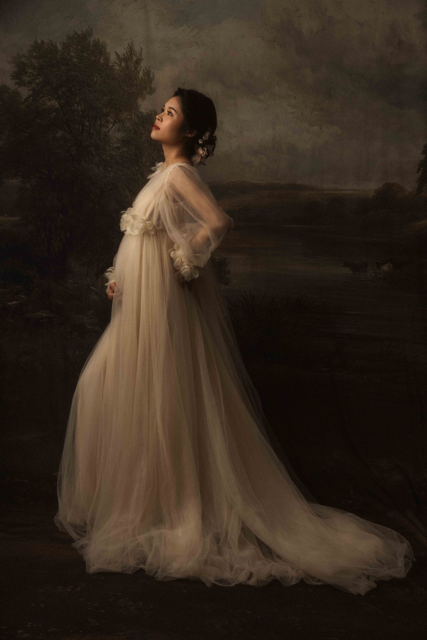 Romantic maternity photos featuring billowing ivory tulle gown against moody backdrop.