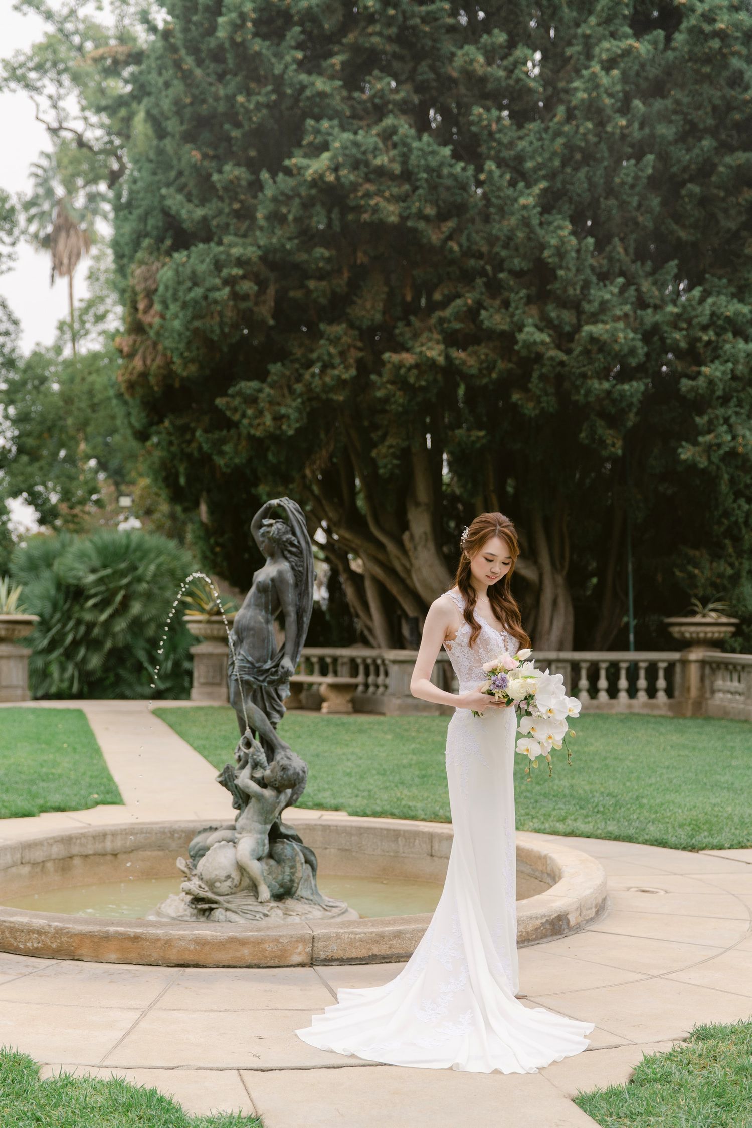 A wedding photoshoot in a garden setting with stone sculptures and lush greenery.