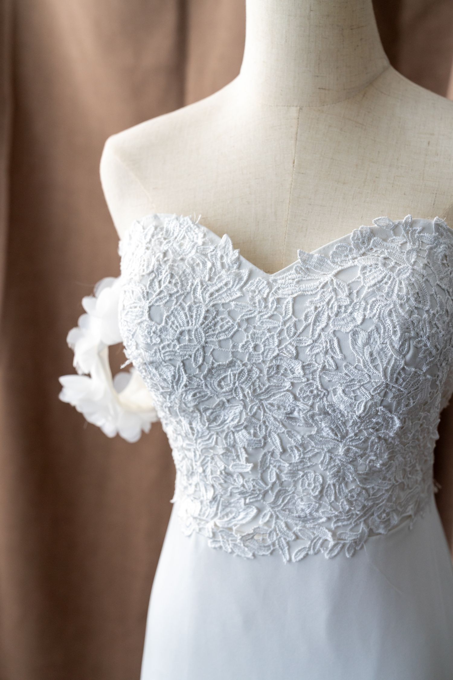 White lace bodice detail of a wedding dress shown on mannequin form.