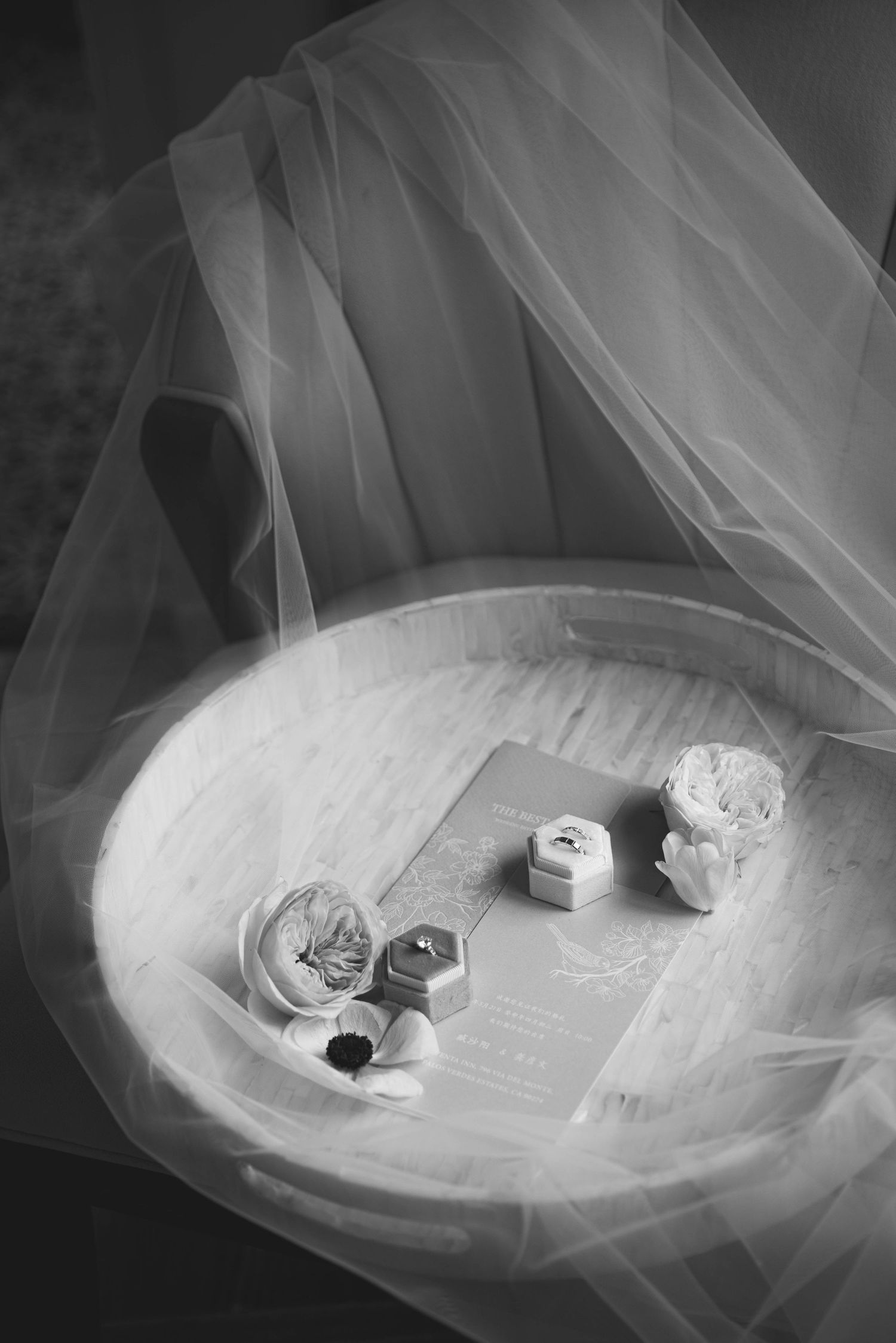 Black and white photo of wedding rings and delicate details arranged on tulle fabric.