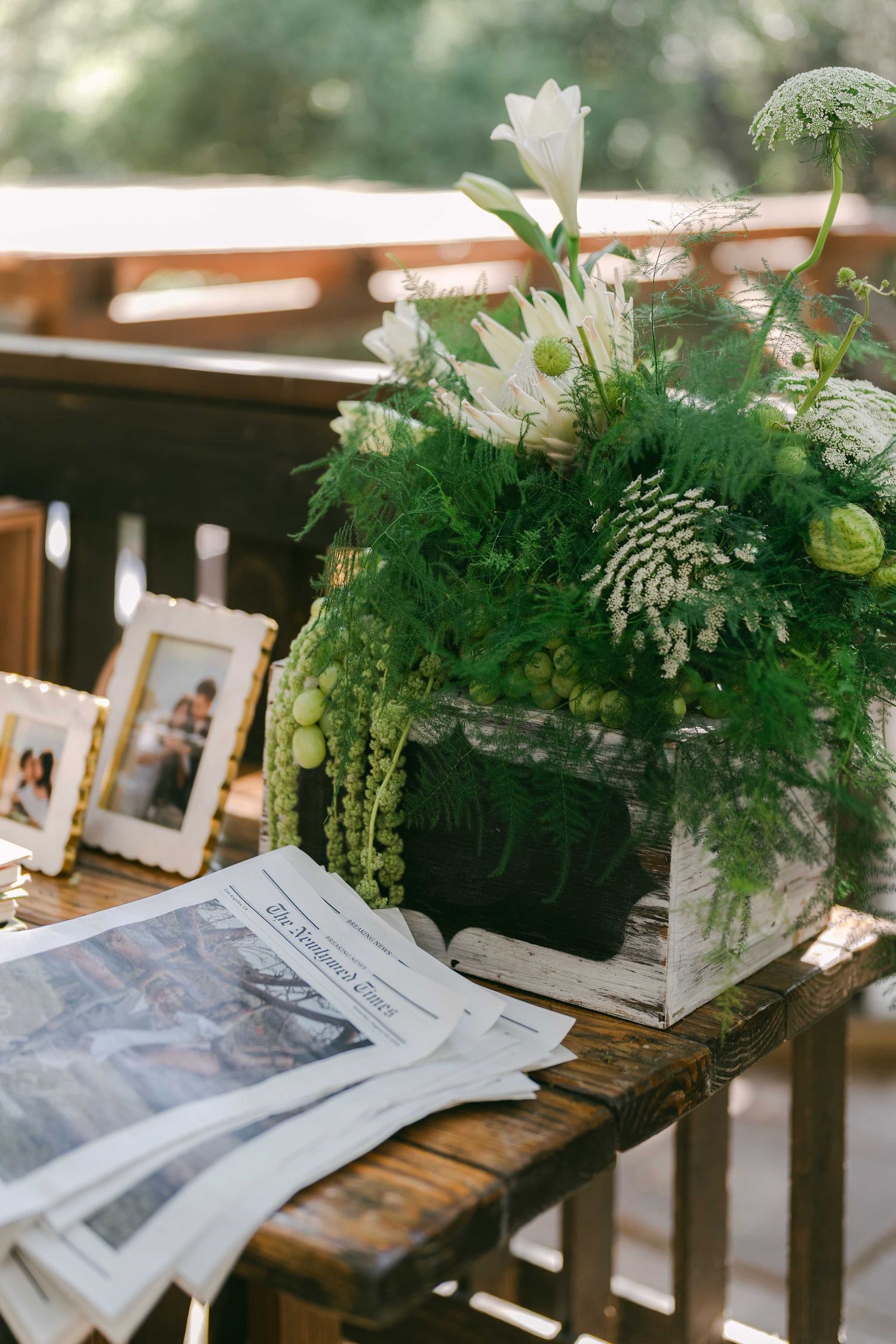 Rustic wooden table with vintage photographs and lush green floral centerpieces.