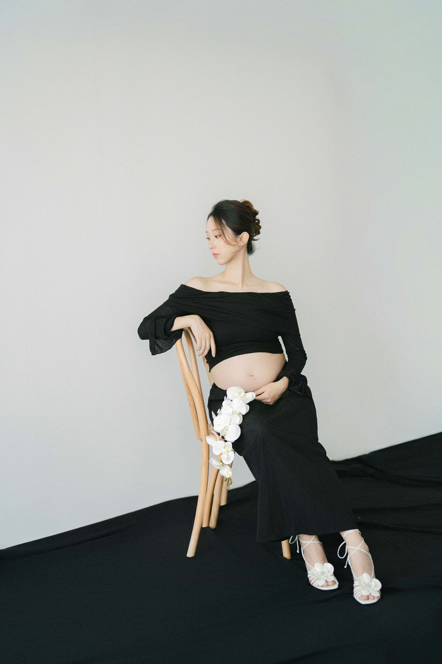 Artistic maternity photos in black dress with white flowers and wooden chair.